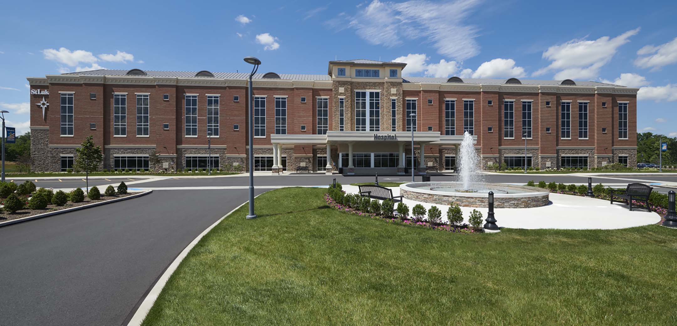 The exterior of the front St Luke's Quartertown red brick building showcasing the front driveway, entrance and front fountain with benches.