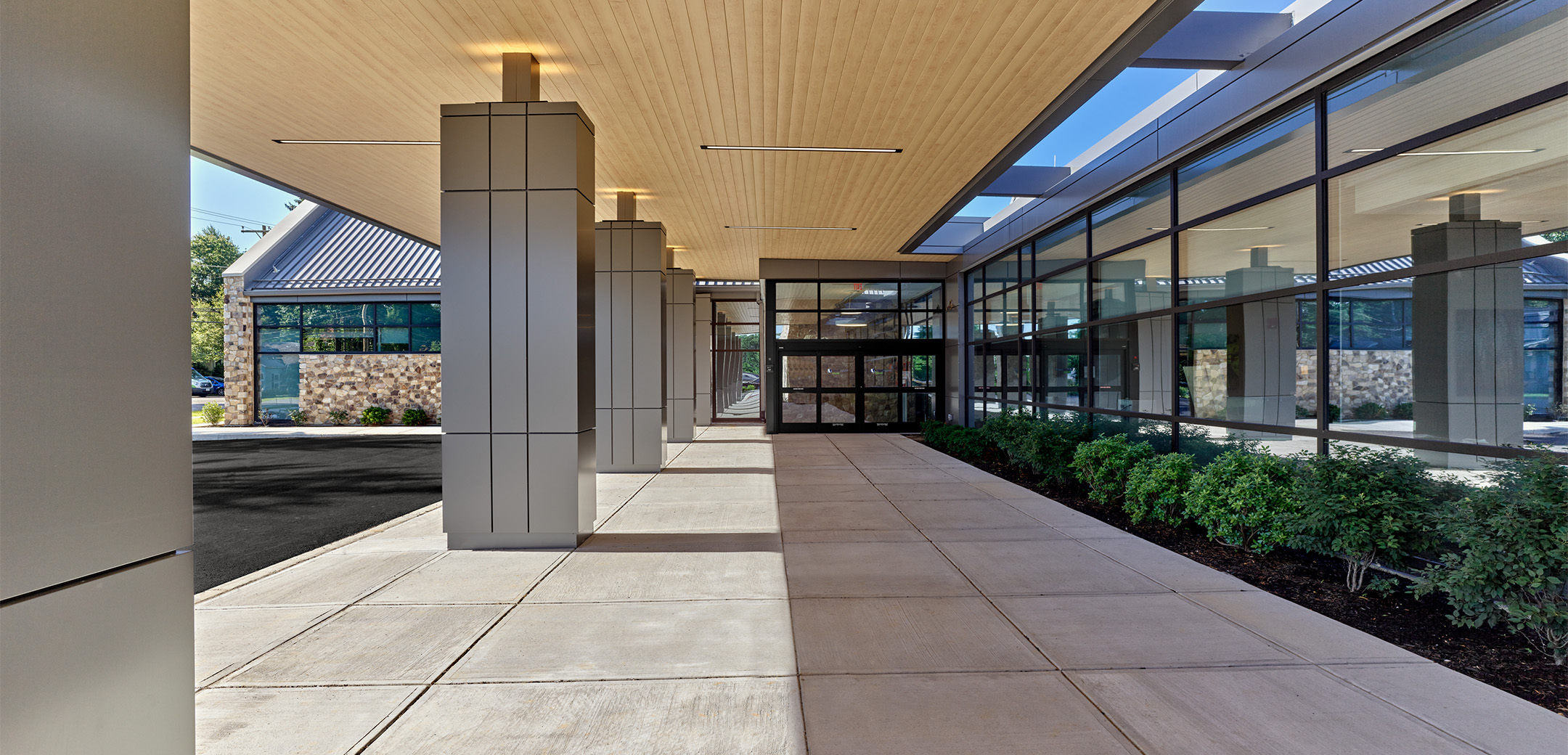 The exterior view from under the portico of the Astoria Health Building showcasing the pillars to the left and glass entrance to the right.