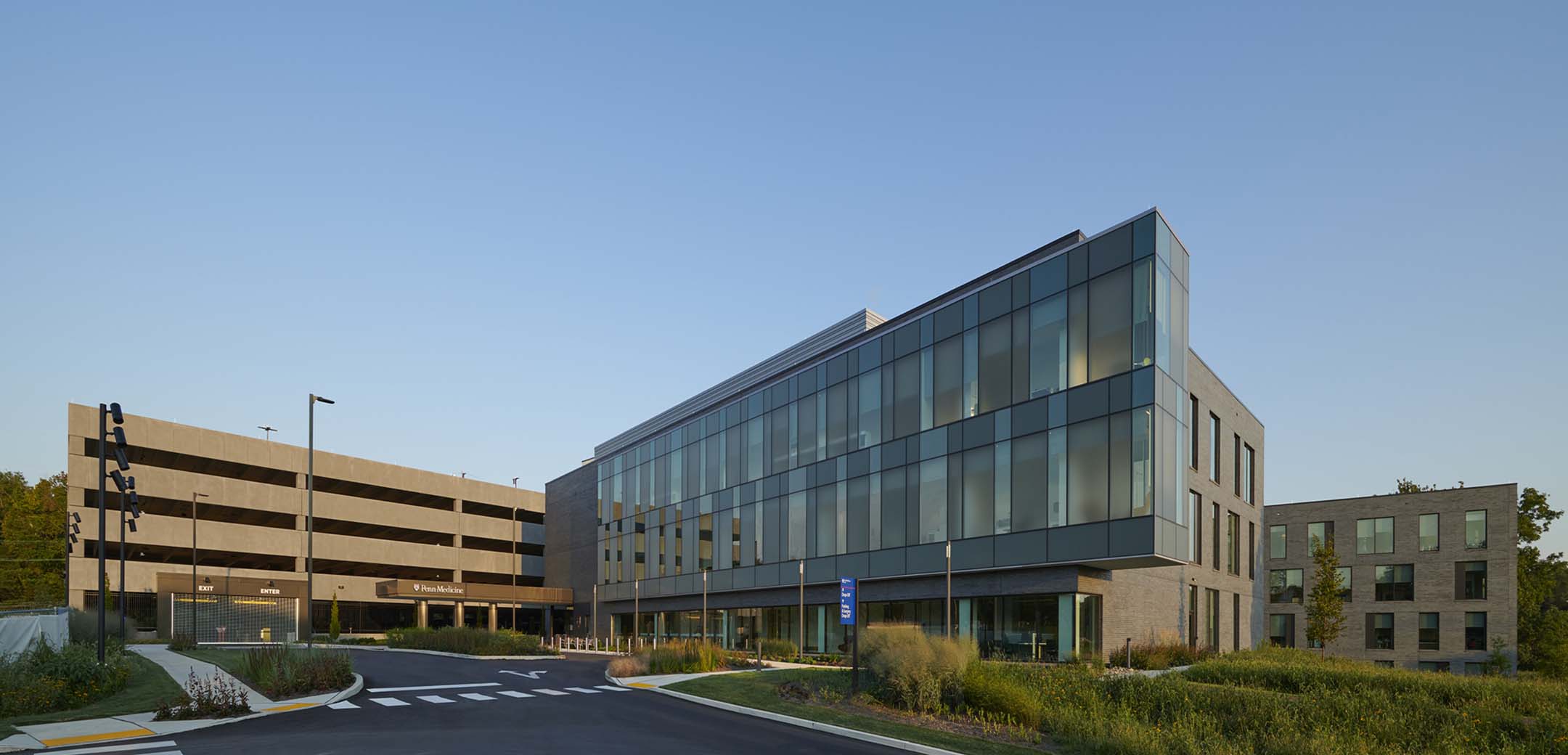 An angled view a modern 3 story Penn Radnor Advanced Outpatient Care Center building showcasing the full length glass window and front driveway entrance.