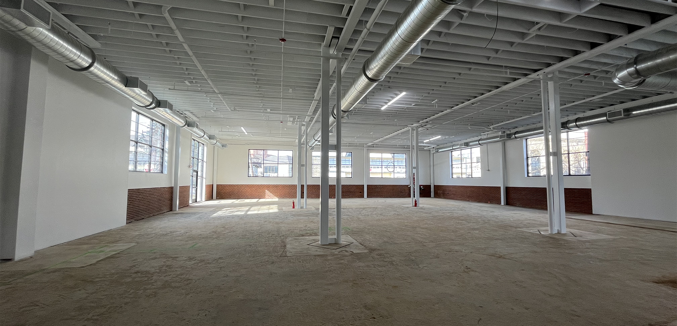 An interior view of the 108 Wayne Ave with tall industrial ceiling, support pillars, white walls and concrete flooring,