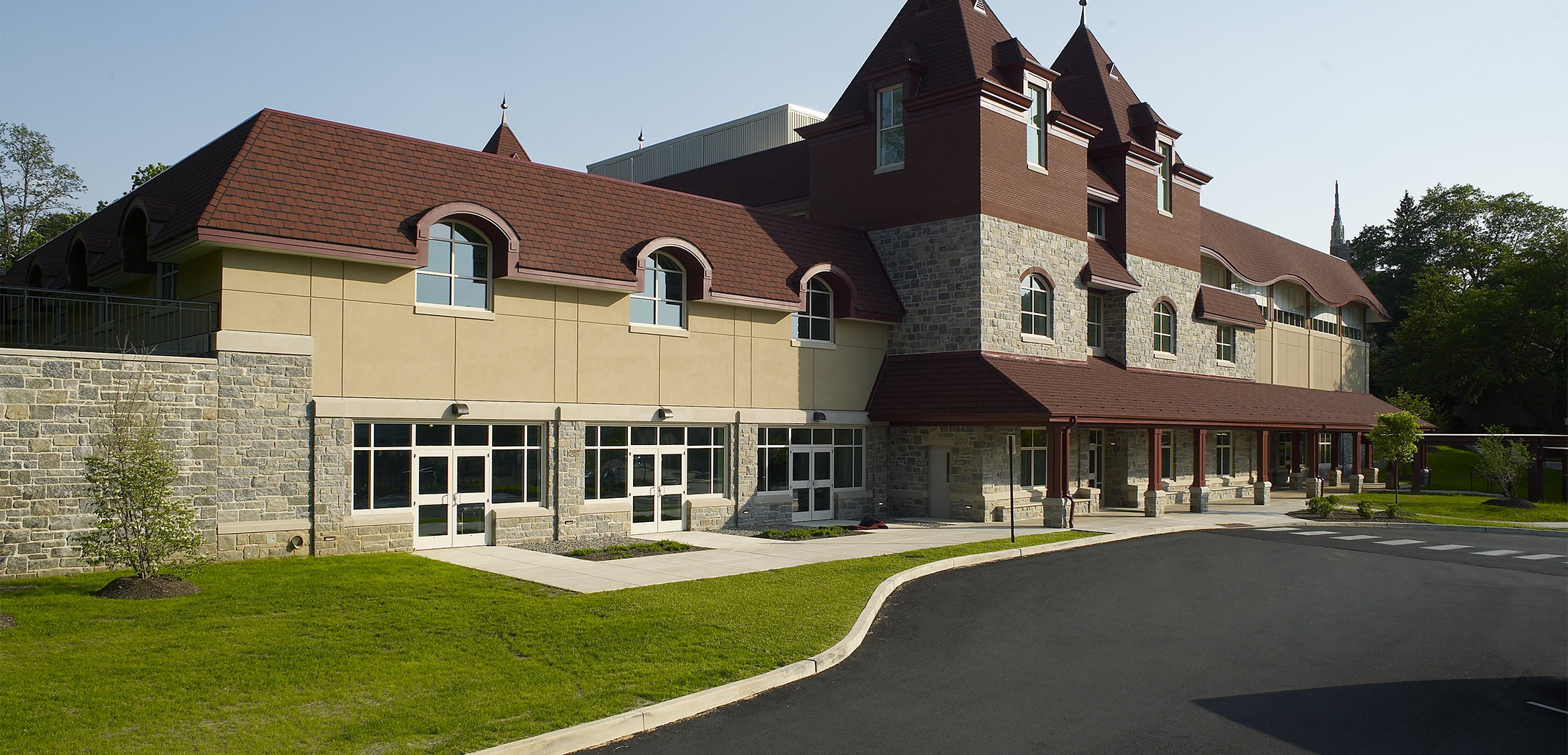 The exterior of the Baldwin School building with stone walls and red shingle roofing, showcasing the multiple front entrances, driveway and front lawn.