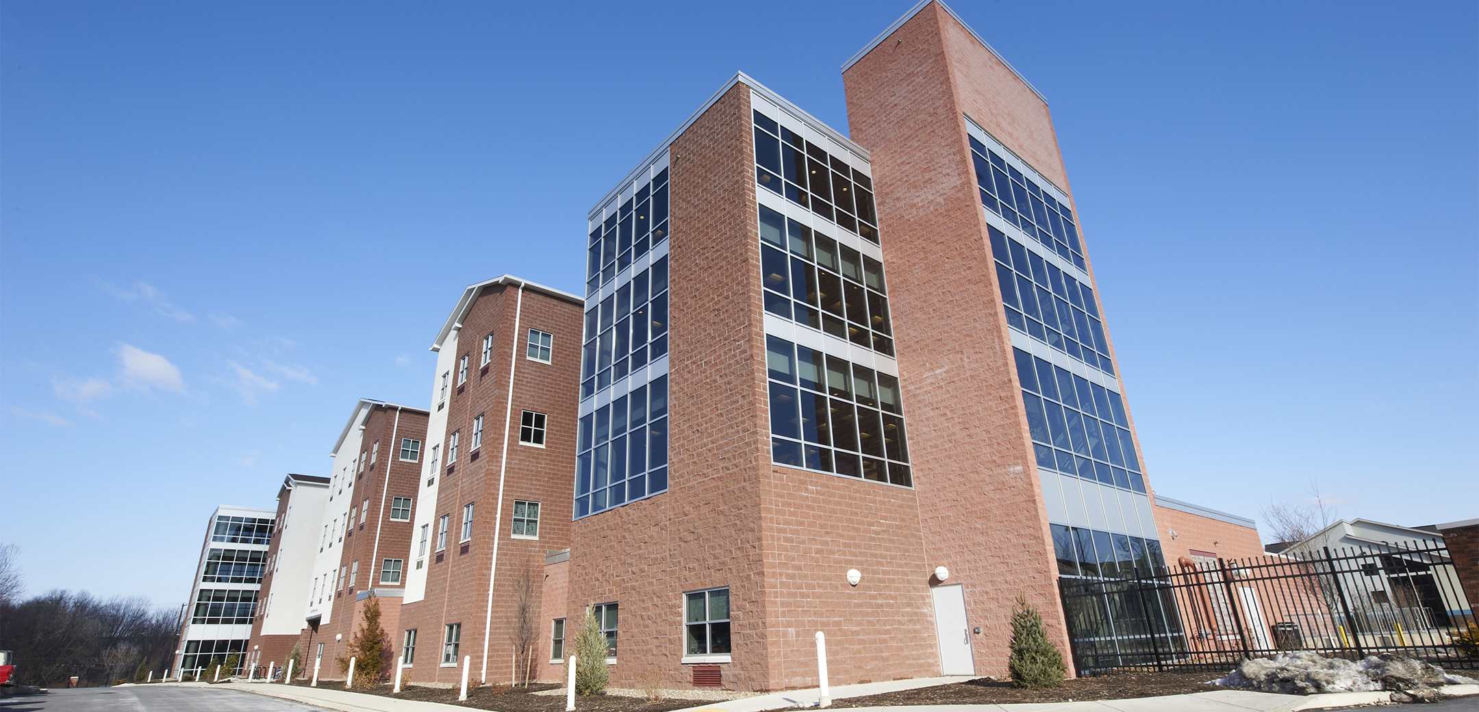 The exterior of the Stage x PA College brick building with three story height glass window accents, showcasing the front driveway and gate.