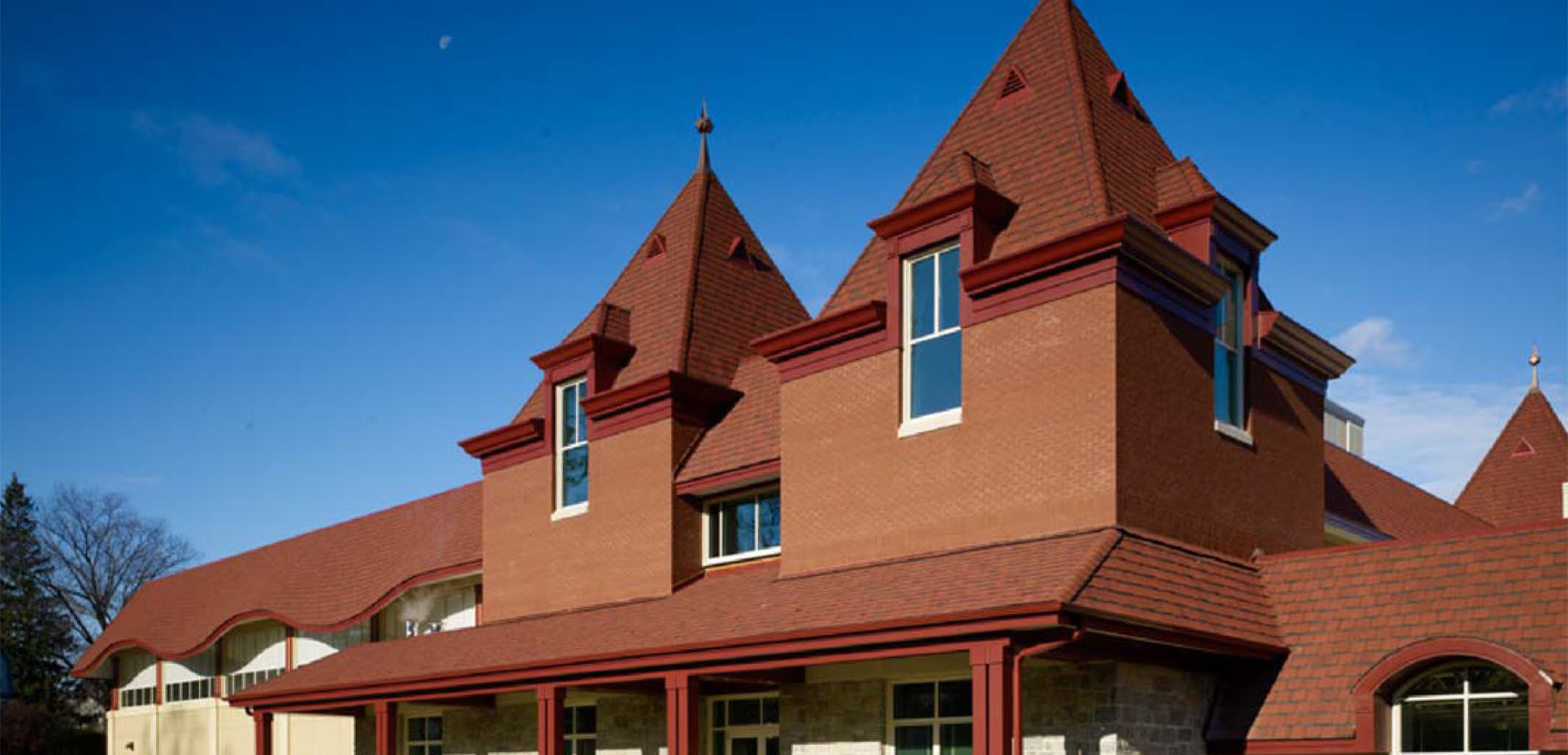 An angled exterior view of the Baldwin School stone, red brick and shingle roof design back side and back grass lawn in the foreground.