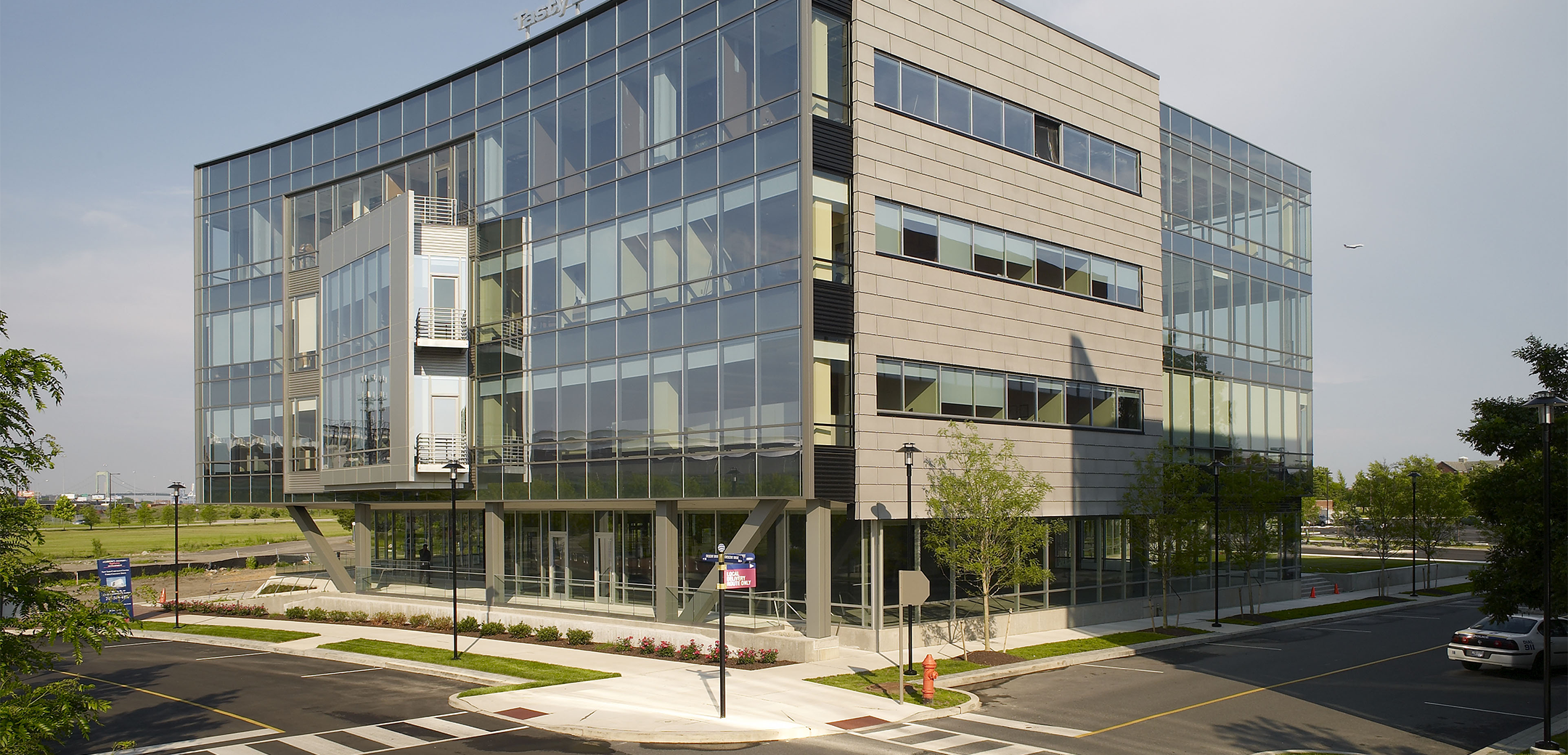 A view of a 4-story Tasty Baking company headquarters building with a full glass wall layering the front side, showcasing the street parking and intersection.