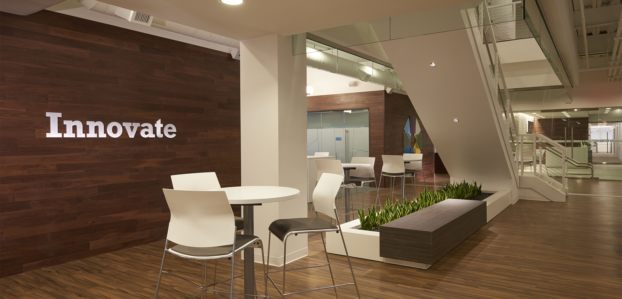 The interior space of Amerisource Bergen featuring an upwards staircase and lobby seating in a wood floors and accent environment next to an Innovate sign on the wall.