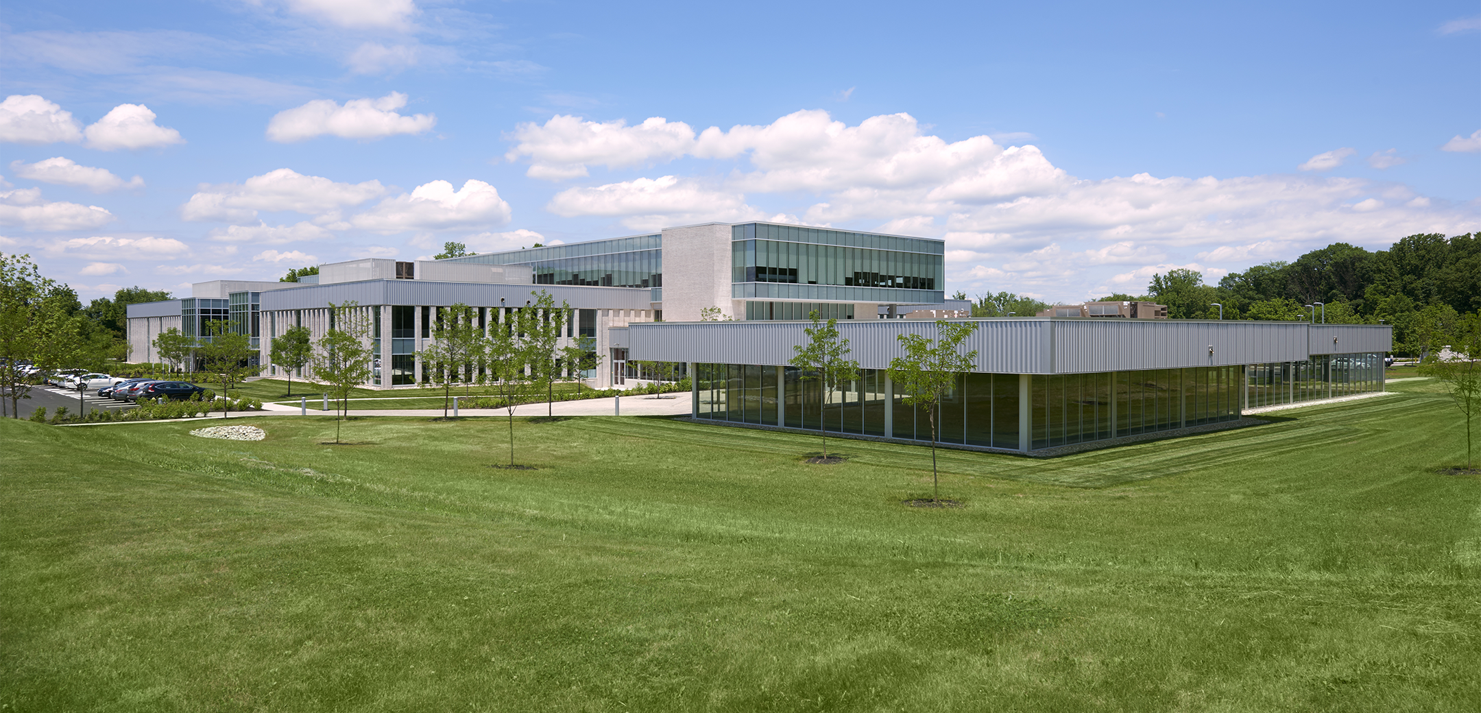 An angled view of the back of Arborcrest Corporate Campus featuring a two story, modern, office building with full-height glass cladding and landscaping in the front.