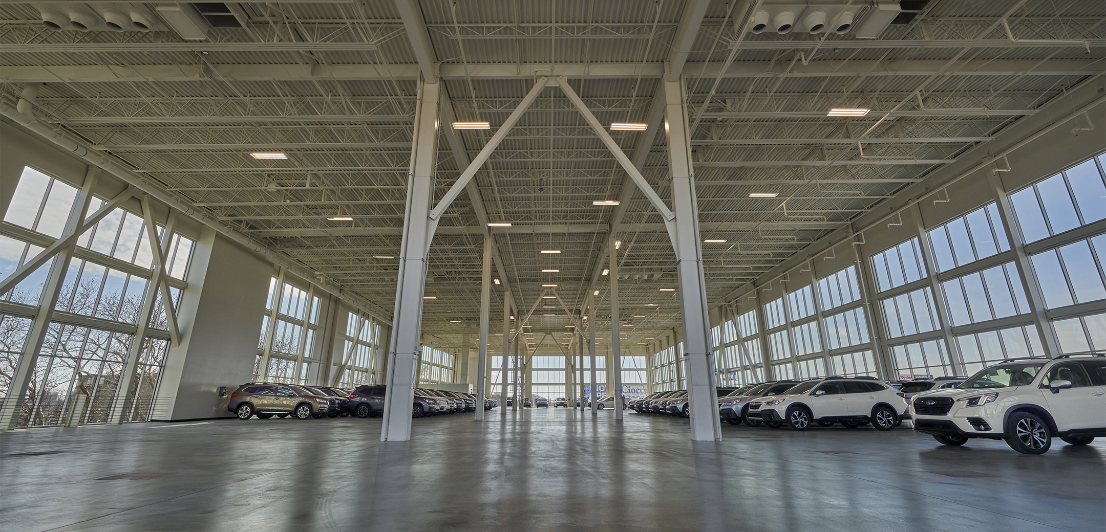 The interior view of the Ciocca Subaru building with tall ceilings, glass panel windows, metal support pillars and cars lined upon along the walls.