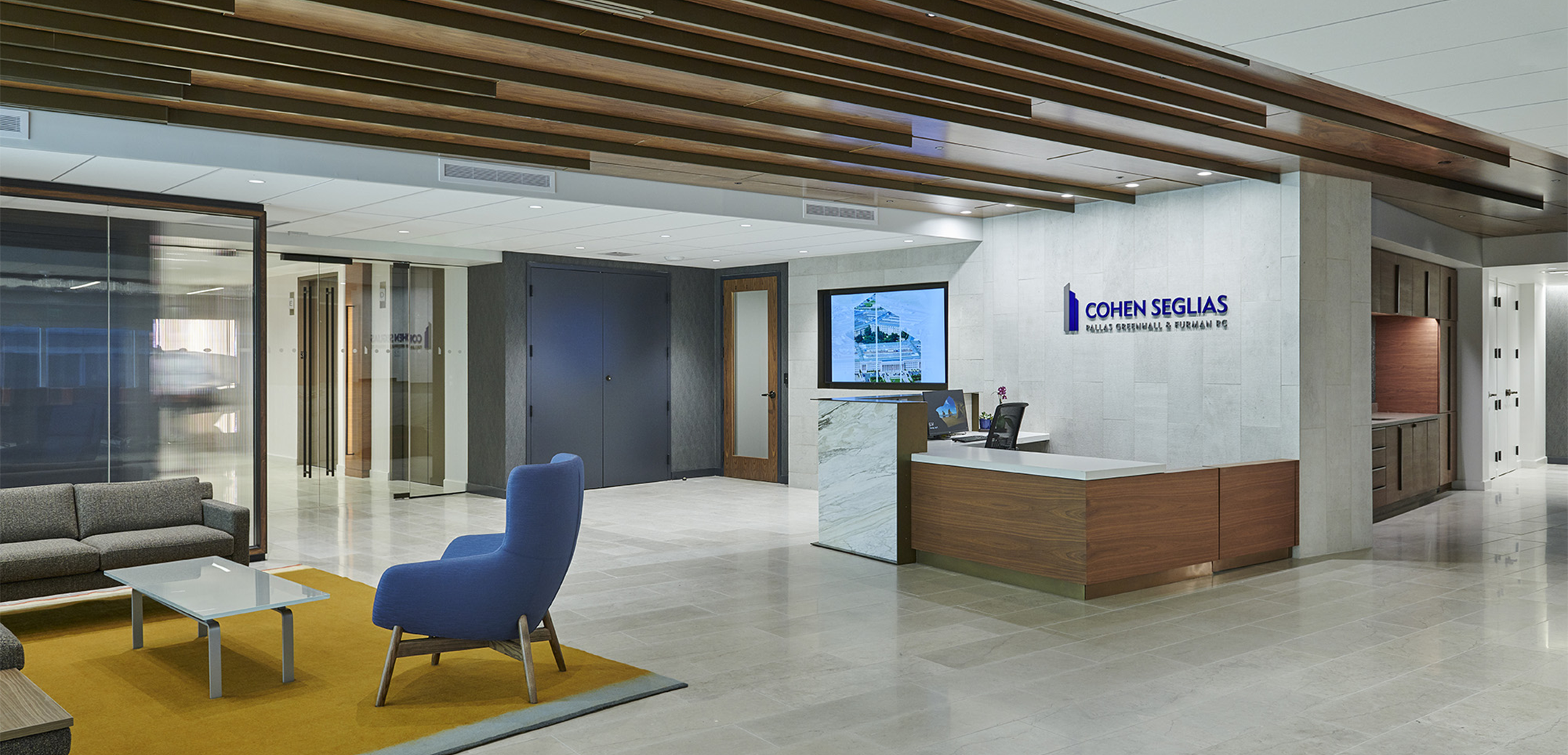 An interior view of the Cohen Seglias lobby and waiting area showcasing the marble and wood reception desk, couches and glass coffee table on the right side.