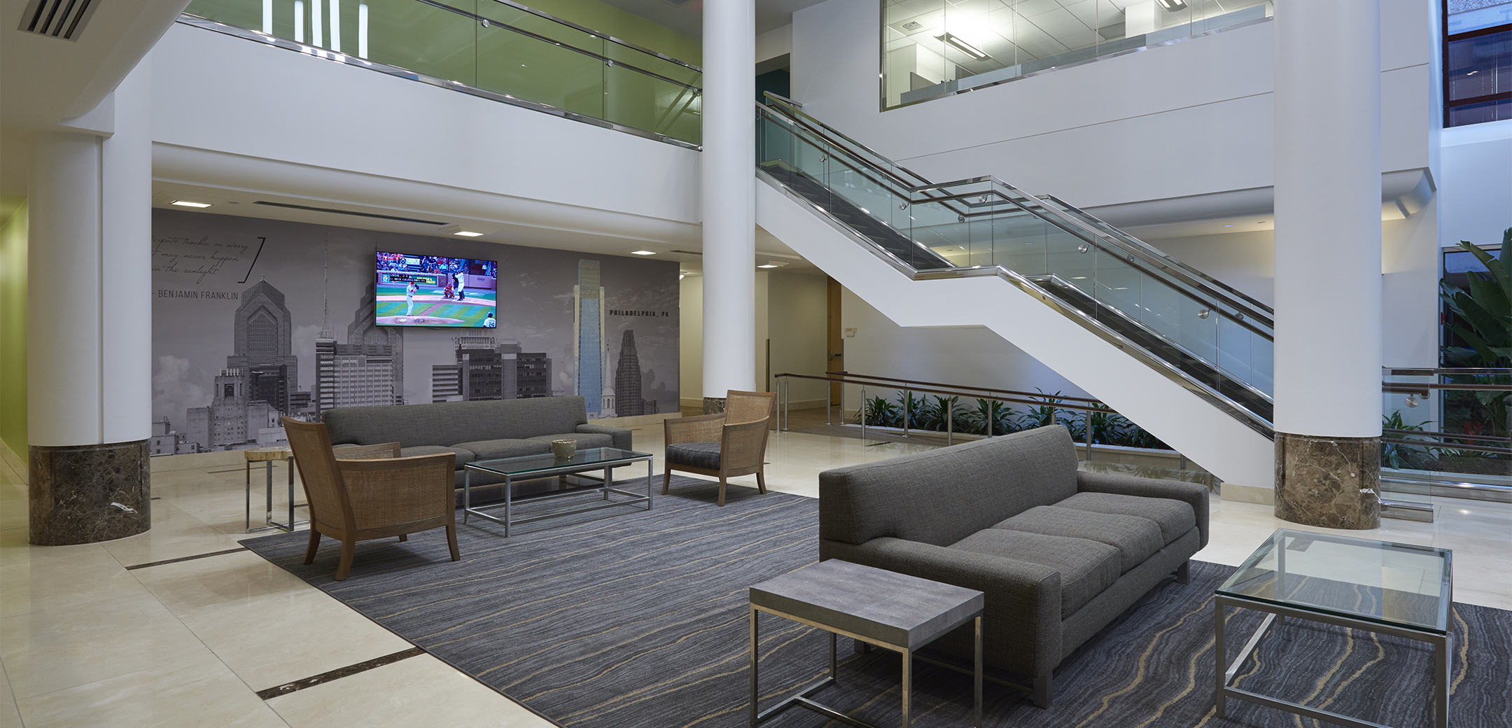The empty lobby of Comcast Communications Spotlight with a long staircase connecting the two floors, a sitting area in the front, and Philadelphia skyline mural on the back wall.
