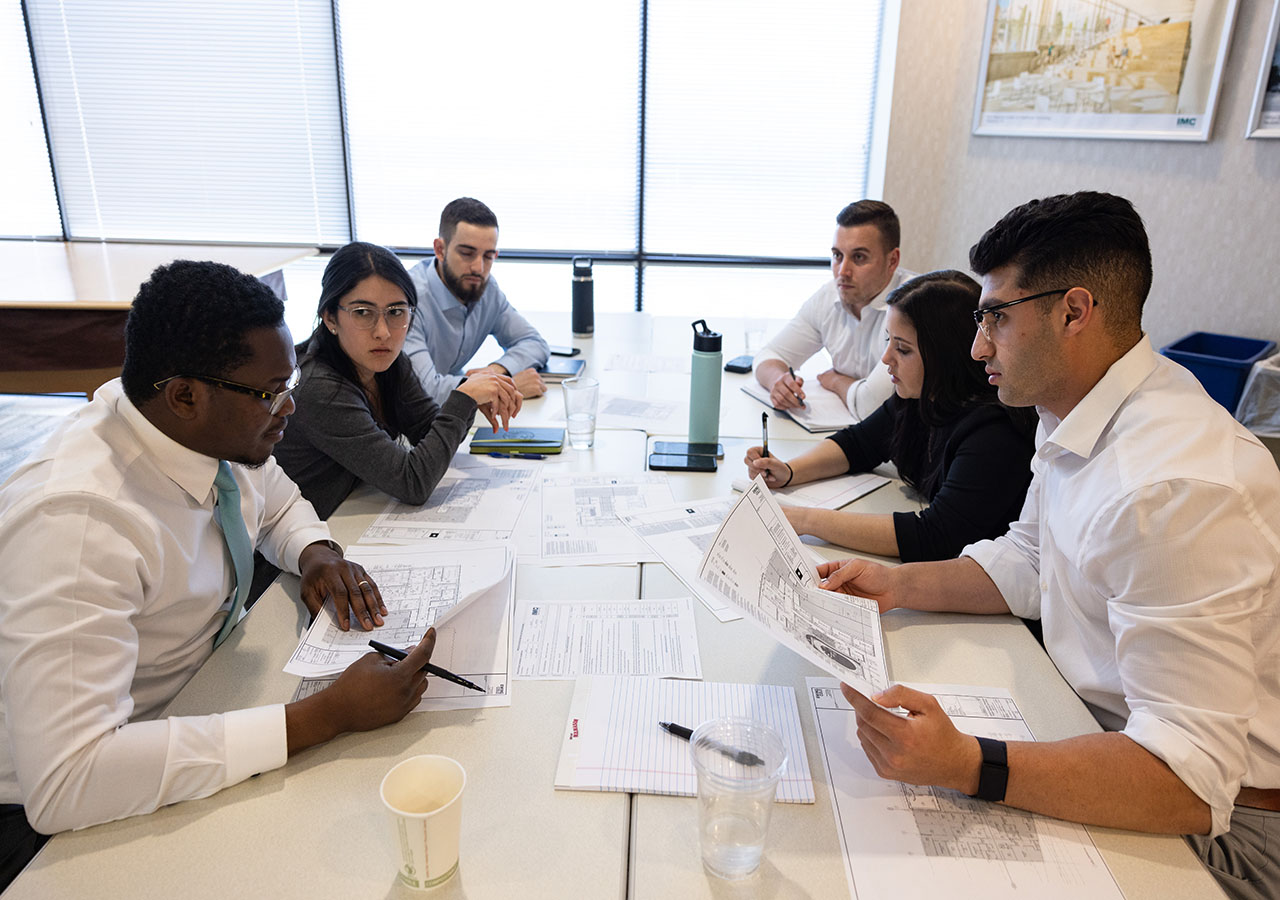 A group of IMC employees sitting at table discussing the project drawings in their hands.