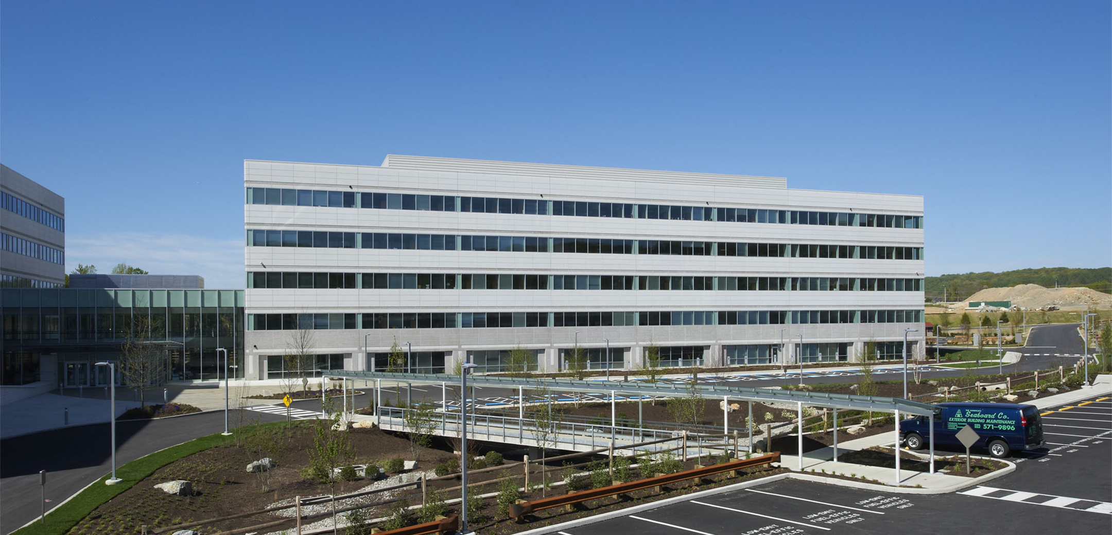 A side view of the 5-story Endo pharmaceutical building showcasing the glass bridge lobby and front parking lot.