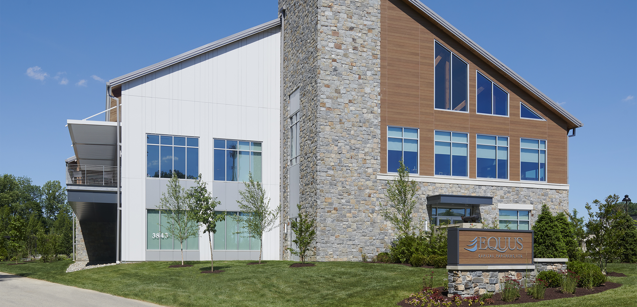 The side view of Equus Capital Partners headquarters office building featuring a mix of stone and wood for the exterior and a wooden sign in the front that reads Equus Capital Partners.