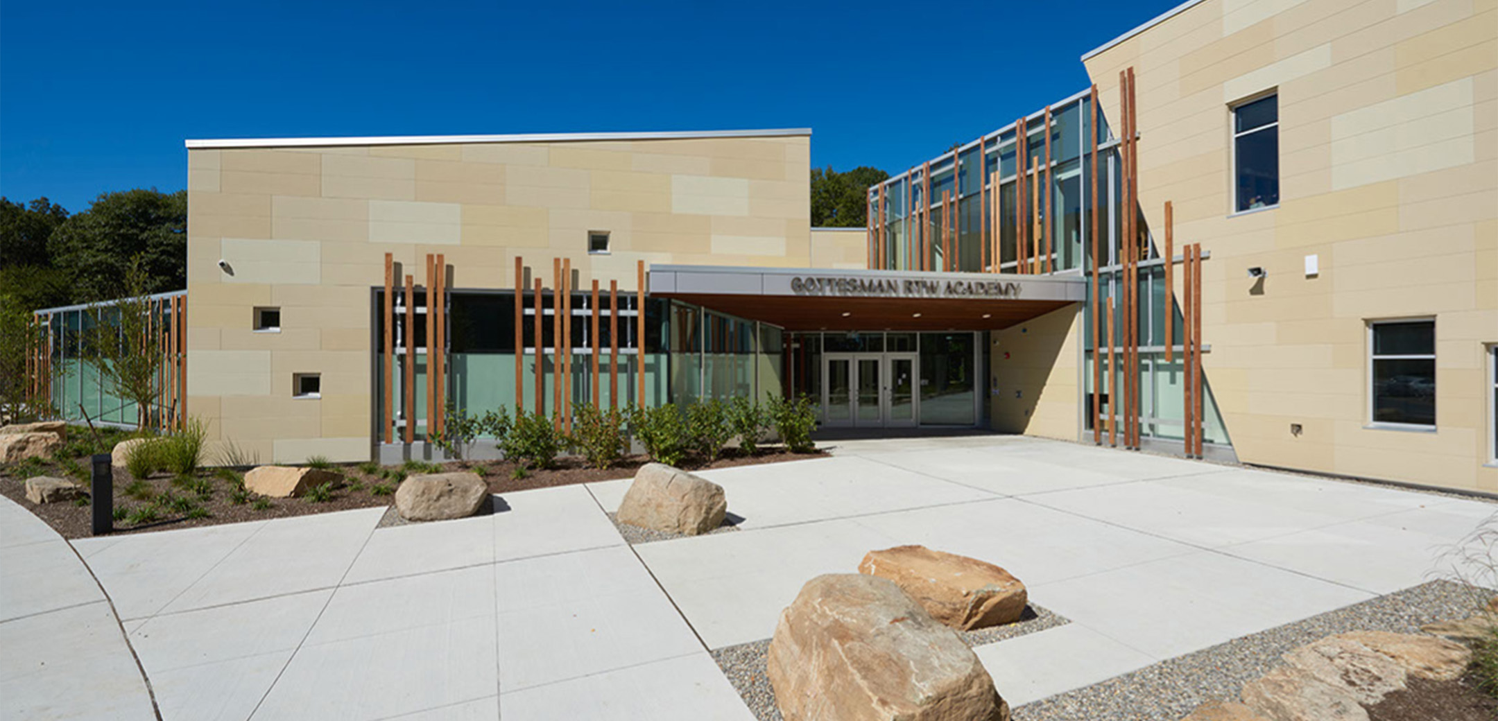 A close up view of the Gottesman RTW Academy building's front entrance with stone décor and wood board glass accents.