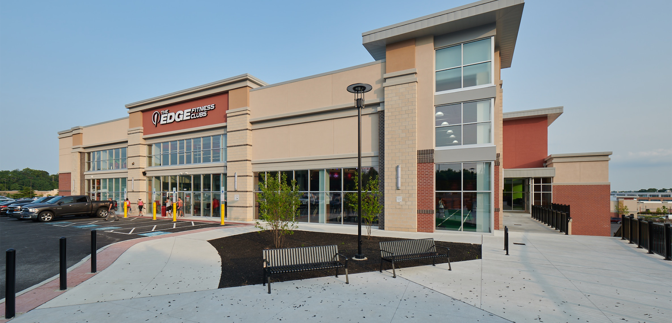 An exterior view of the Promenade at Granite Run building showcasing the glass storefront, entrance, floor to ceiling edge design, parking lot and a large sidewalk with benches in the foreground.