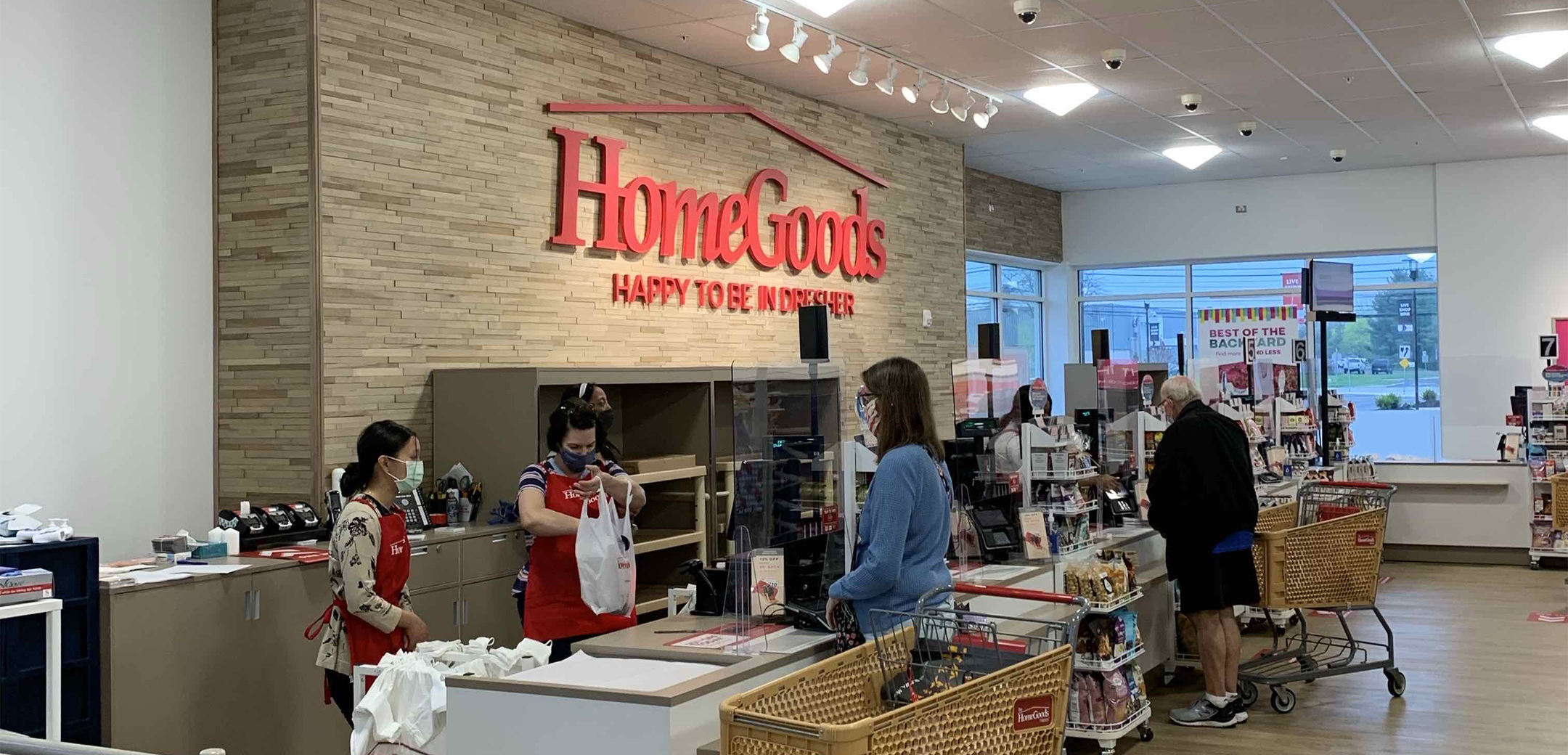 An interior view of the Homegoods checkout counter with a brick accent wall, high ceilings with cameras attached to it and cashiers, customers I the center.
