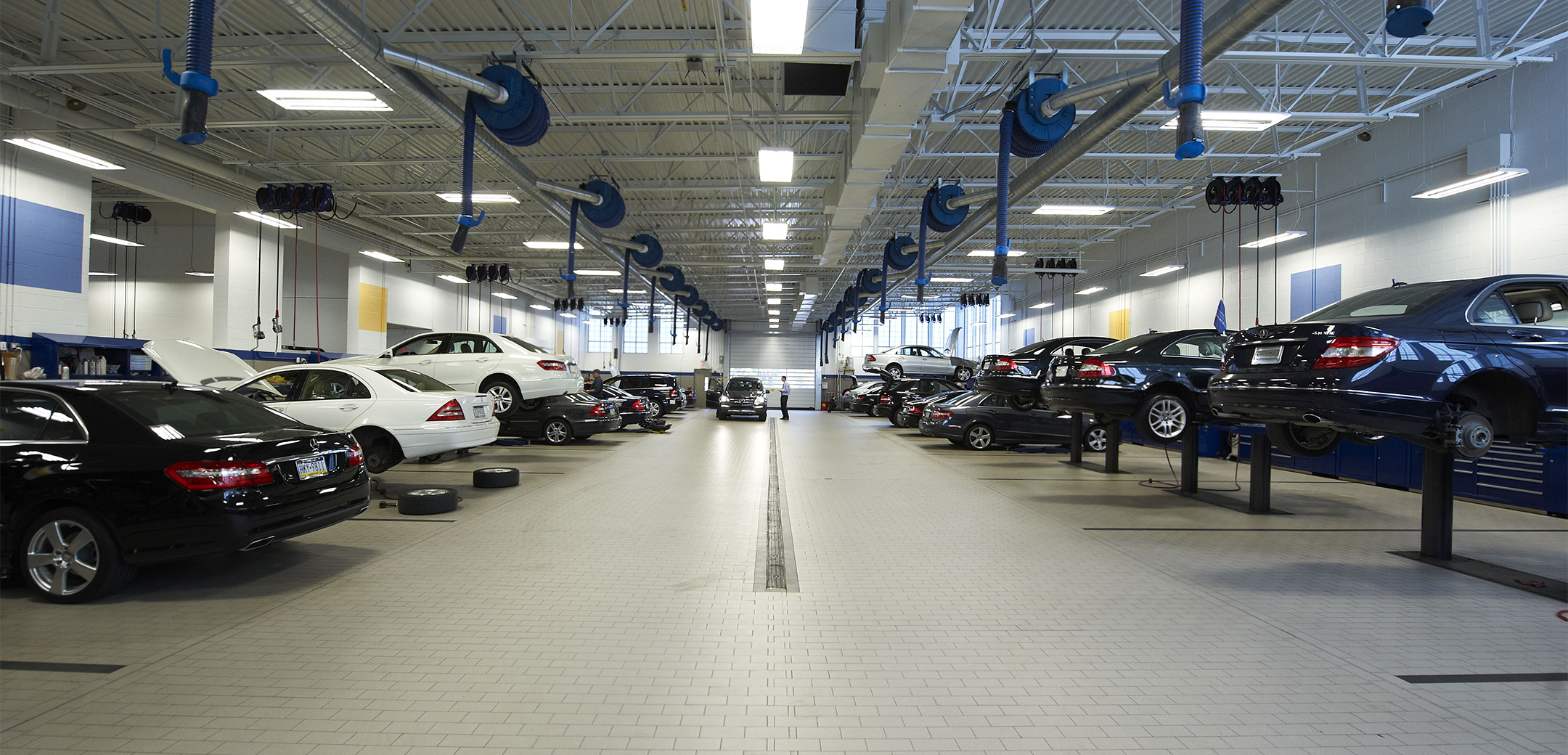 An angled interior view of the Euro Motorcars brick floor, tall ceiling with an adjustable vacuum system and cars on both left and right side lined up along the wall.