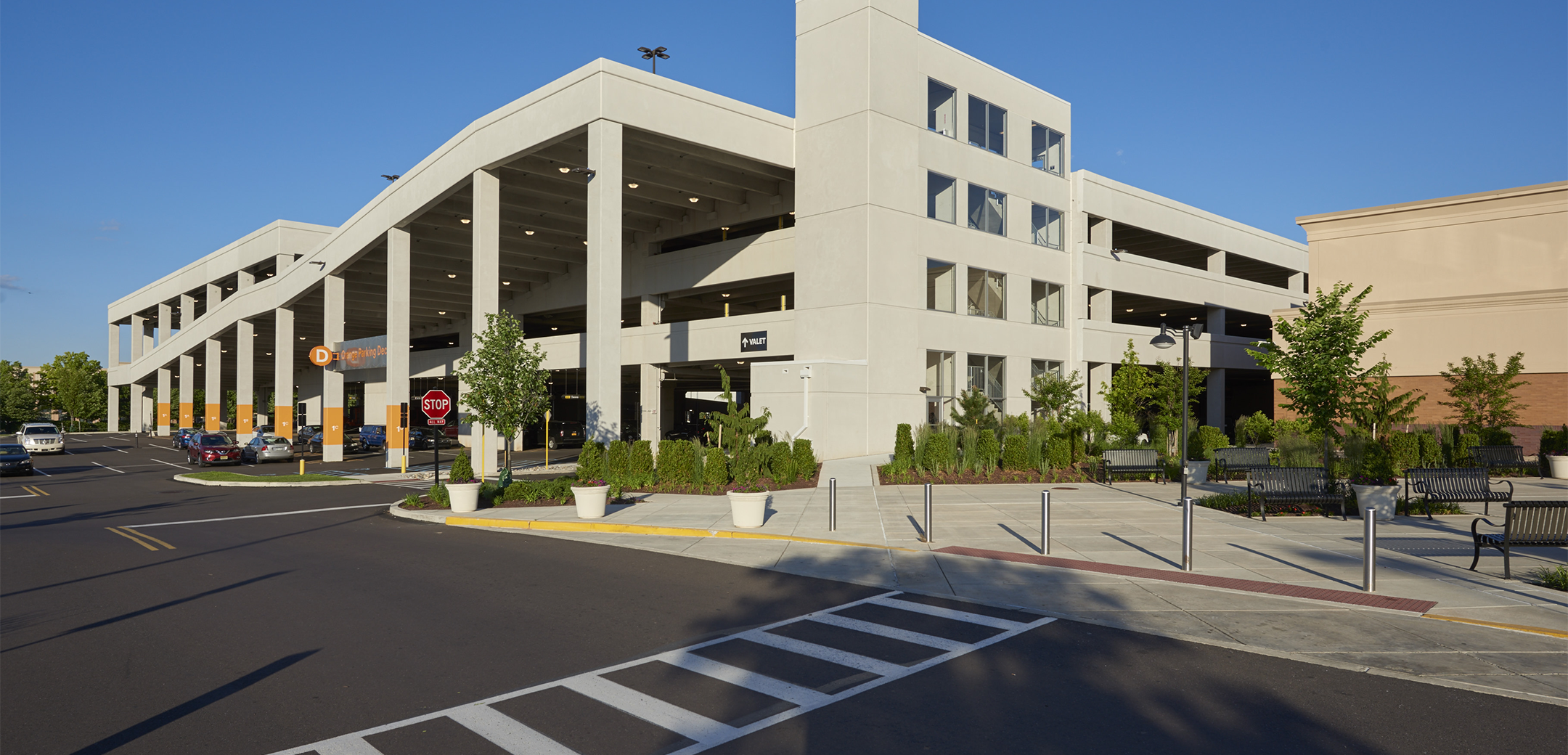 The exterior of the KOP Expansion parking lot building, showcasing the three stories, support pillars, ramps going up to the higher floors and driveway in the foreground.