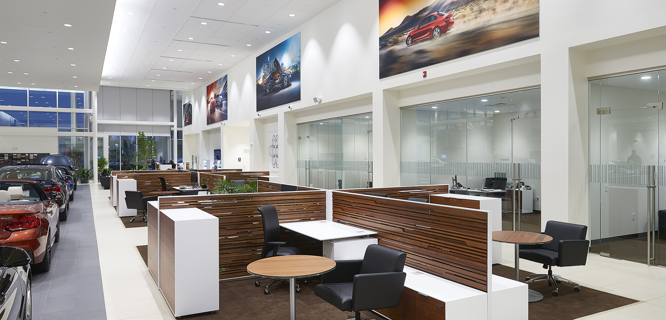 An interior view of the Ottos BMW sales floor area showcasing the glass window cubicles, wooden accented customer cubicles and cars lined along the side.