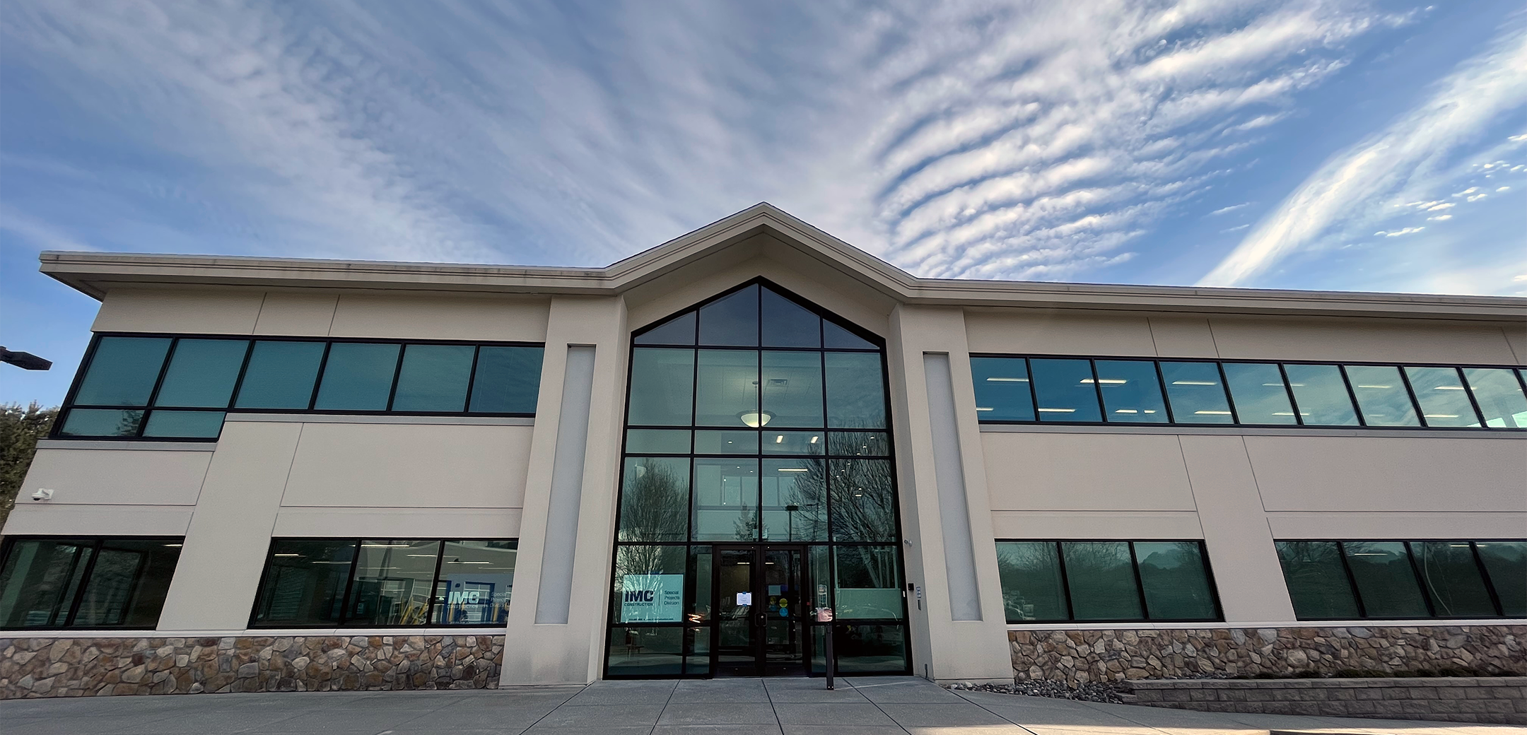 An exterior view of the PA Leadership Charter School showcasing the story triangle end glass front entrance with an IMC sign in the windows and main sidewalk leading up to it.