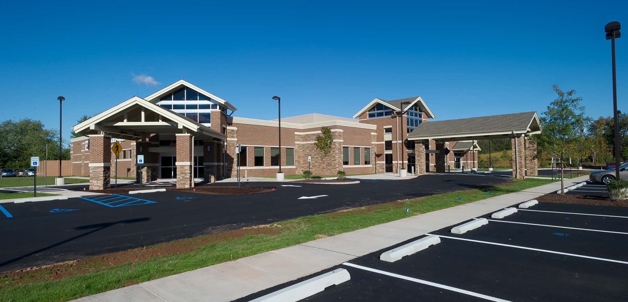 The exterior of the Physician Care Surgical hospital showcasing the red brick design, the main entrance, drive in entrance and large parking lot.