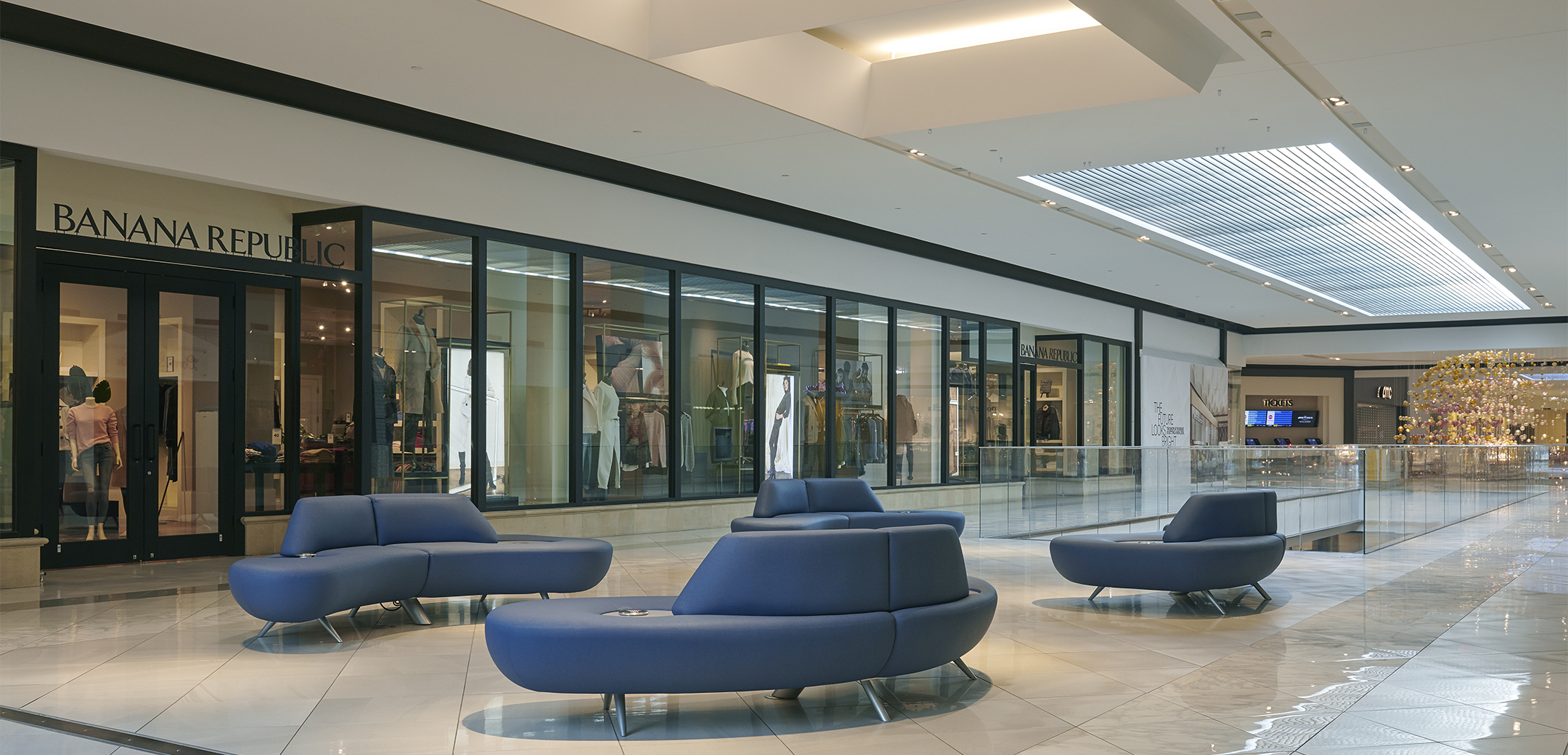 An angled interior view of the Shop at Riverside mall second floor, showcasing the rest seating area, with blue couches, tile flooring and a "Banana Republic" signage storefront in the background.