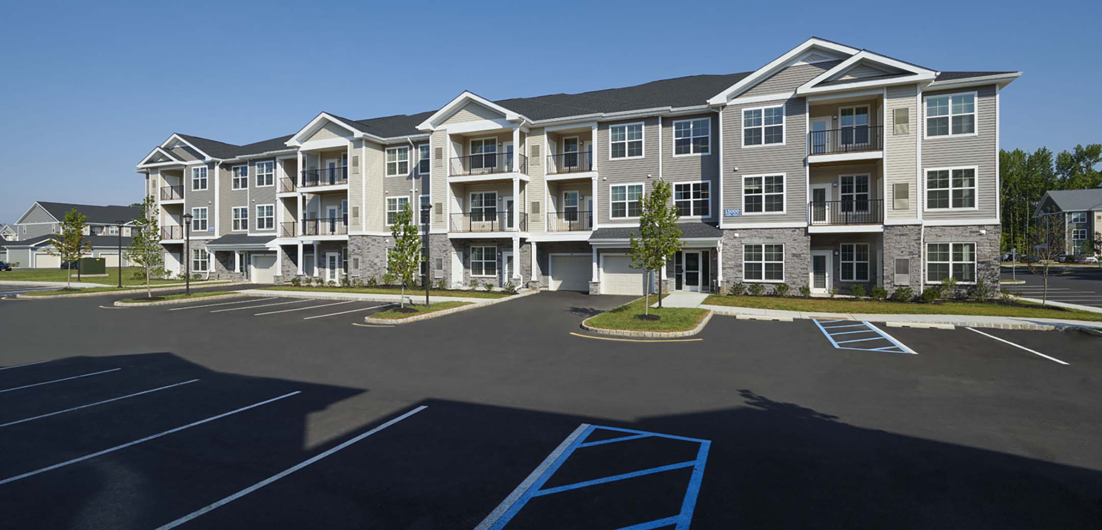 An exterior view of one of the Signature Place MtLaurel apartment buildings showcasing the front garage, front door and parking lot.