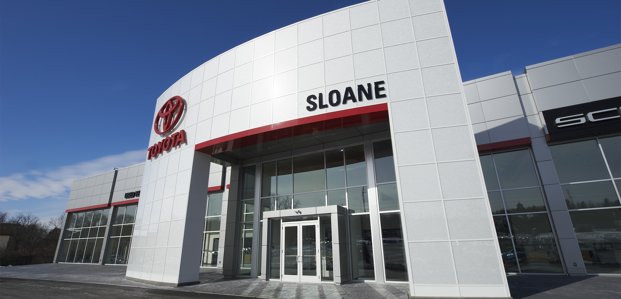 A close up exterior view of the Sloane front entrance, showcasing the glass door, "Sloane" and "Toyota" on the entrance overhang.