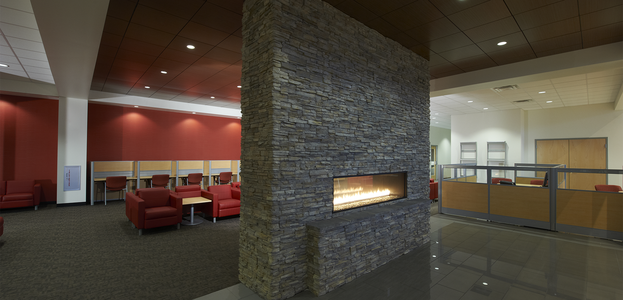 The interior view of the Sloane waiting lobby and sitting area with a brick fireplace in the center and employee cubicles in the background.