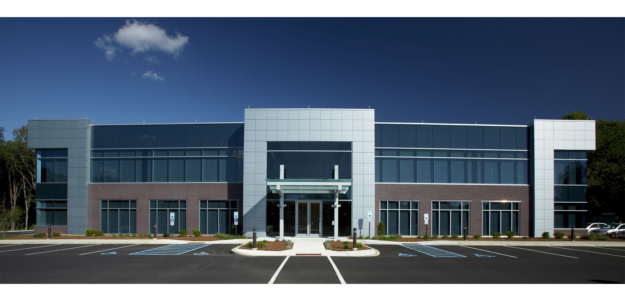The front view of a 2-story South Jersey Federal Credit Union building with multiple shades of gray precast panels and shaded glass windows featuring the front entrance and parking lot.