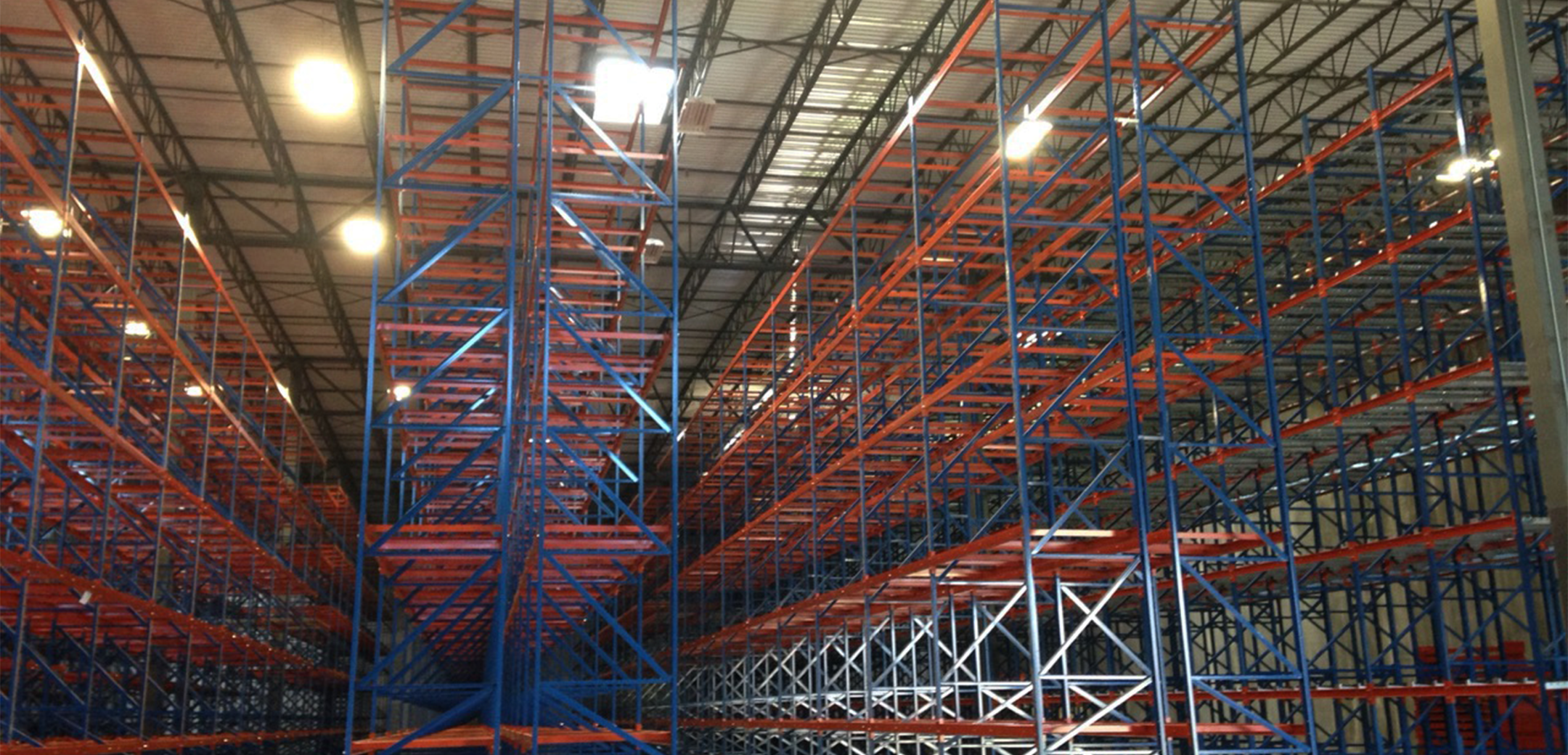 An interior view of the South Washington Park warehouse showcasing the floor to ceiling empty blue and orange colored shelves stretching into the back.