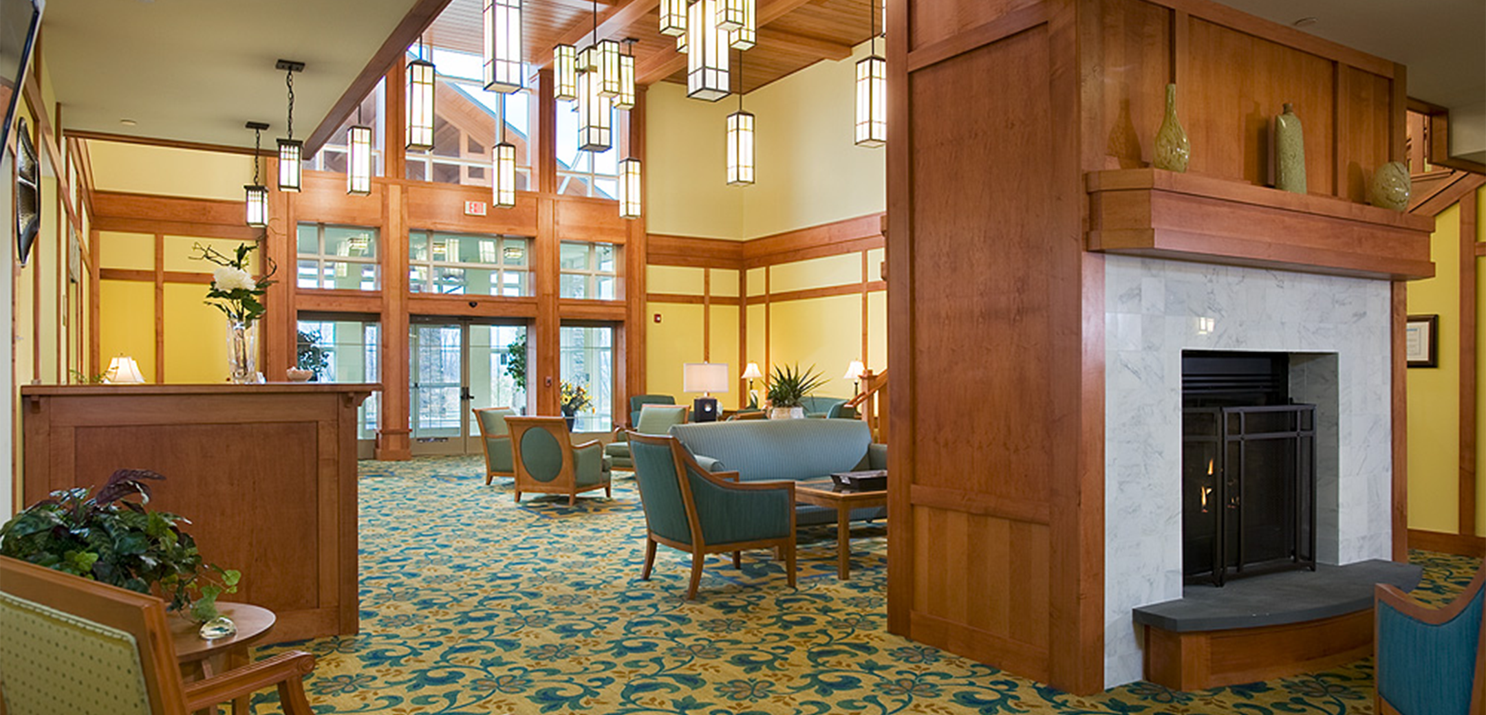 An interior view of the Vantage Point showcasing the lobby reception desk and central wooden pilar with a fireplace and seating in the background.