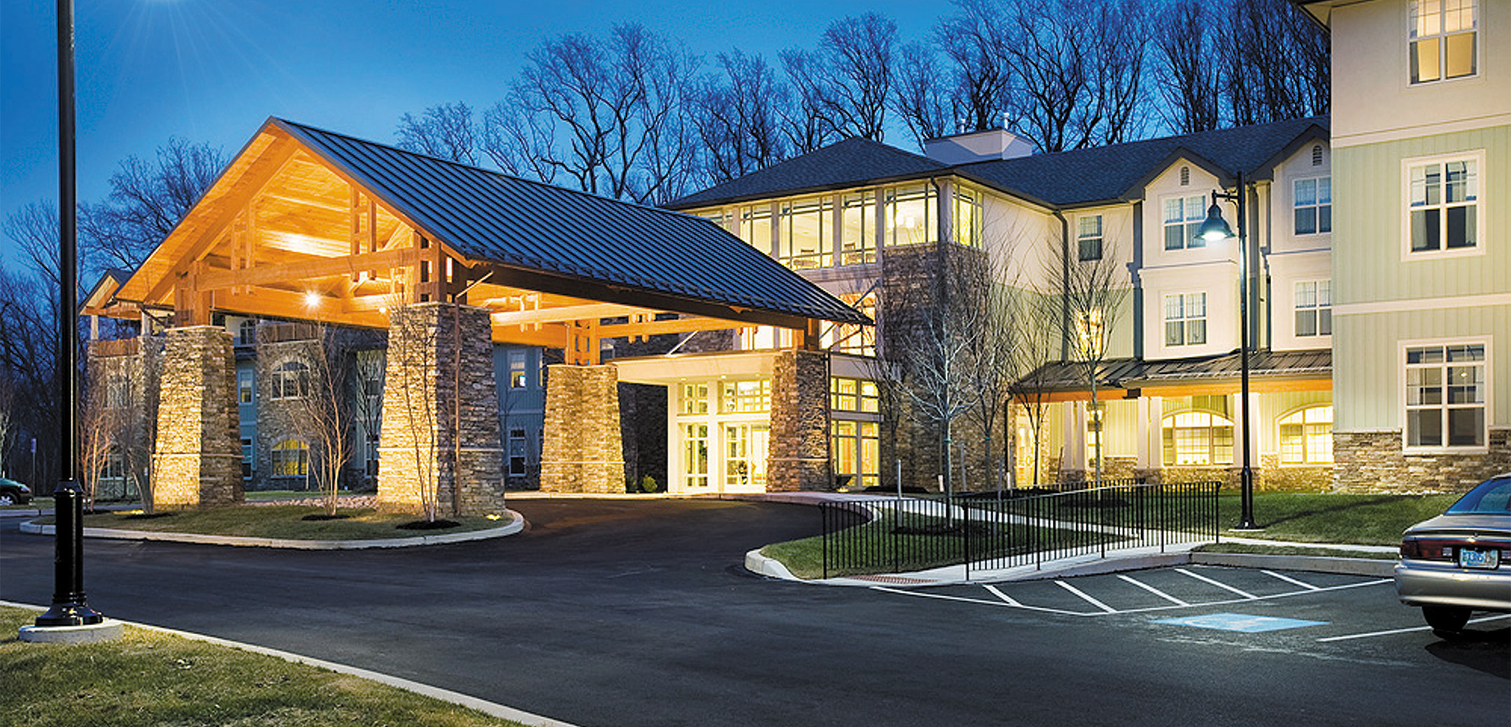 An exterior nighttime view of the Vantage Point front driveway entrance with a wooden structure overhang and stone pillars.