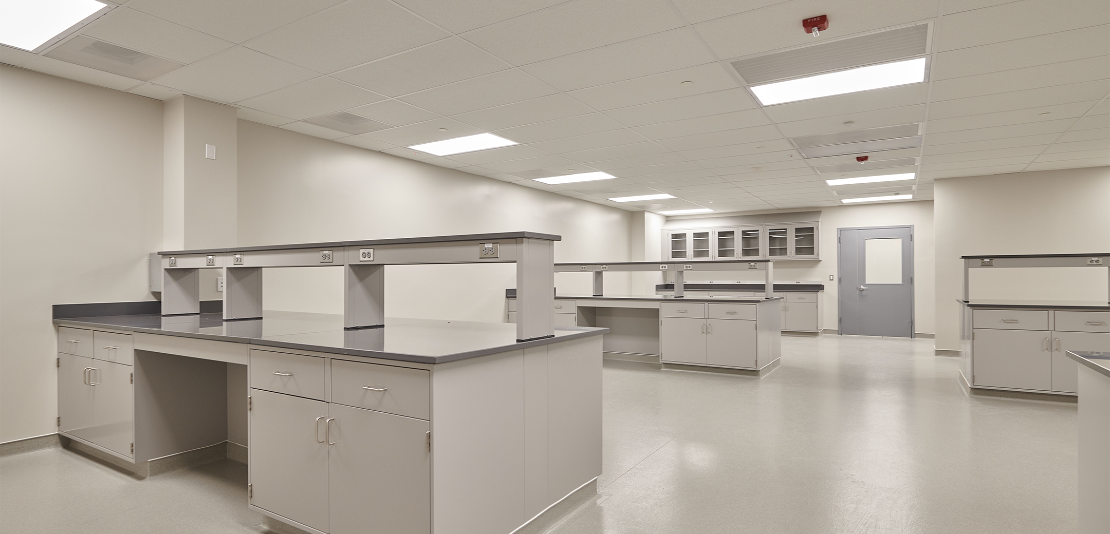 The interior view of Veltek, showcasing the white floor, ceiling and walled room with large workstation tables spread out around.