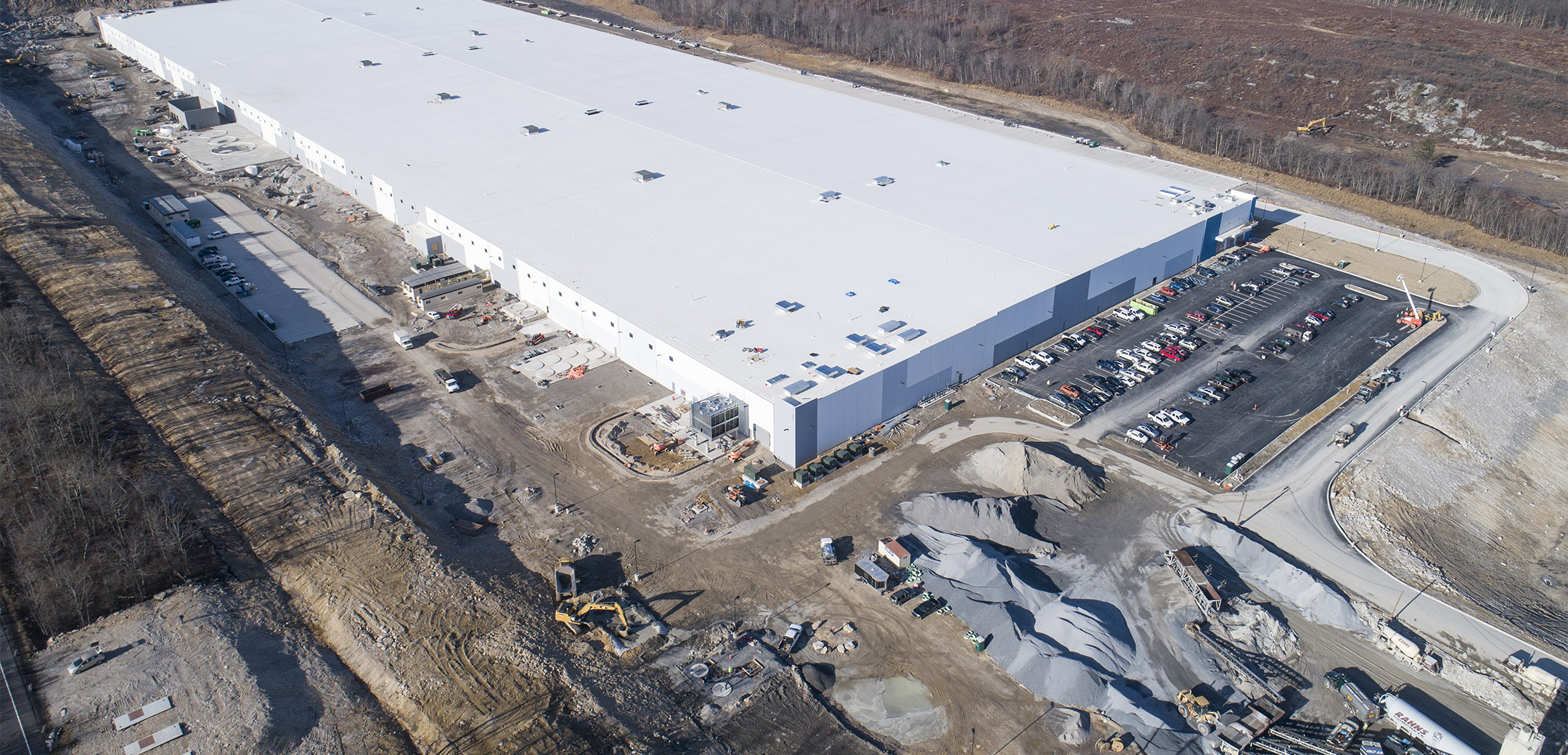 An aerial drone shot of a water bottling industrial facility with white walls and a parking lot in front with cars.