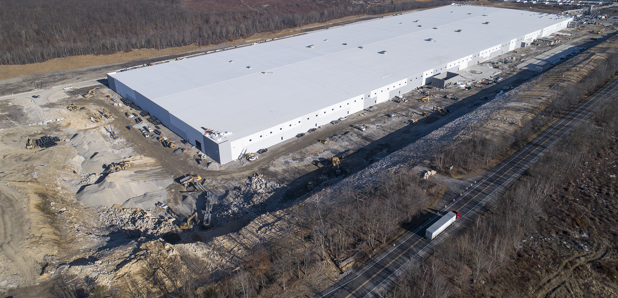 An aerial drone shot of a water bottling industrial facility with white walls surrounding by trees and landscape.