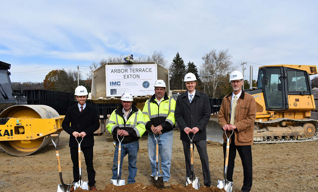 Employees with shovels and hardhats in front of large construction equipment