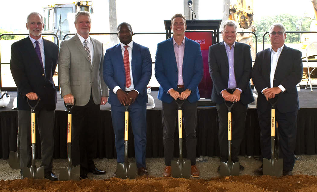 A group of IMC employees posing for a photo with shovels in their hands on a construction site.