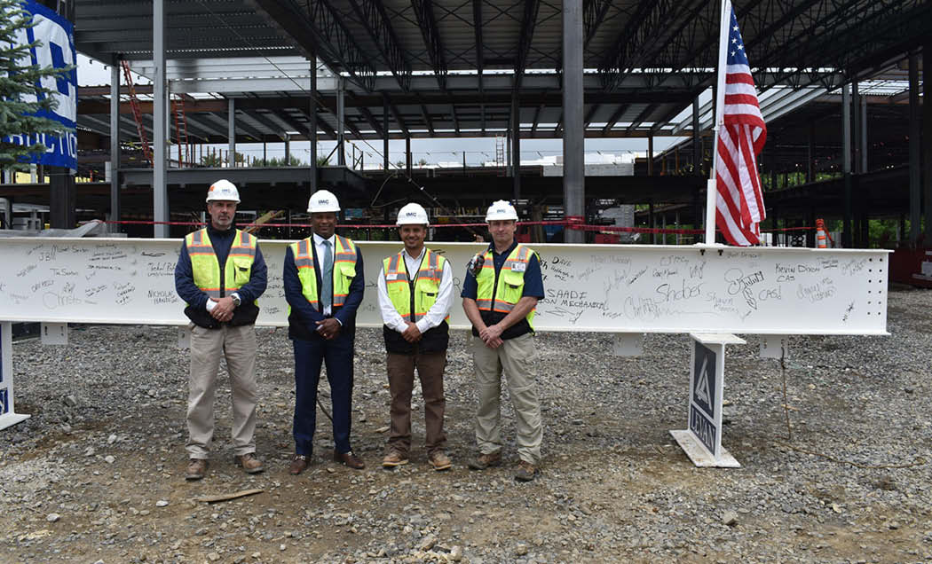 IMC Employees in hardhats and safety vests posing in front of large white beam with signatures and American flag