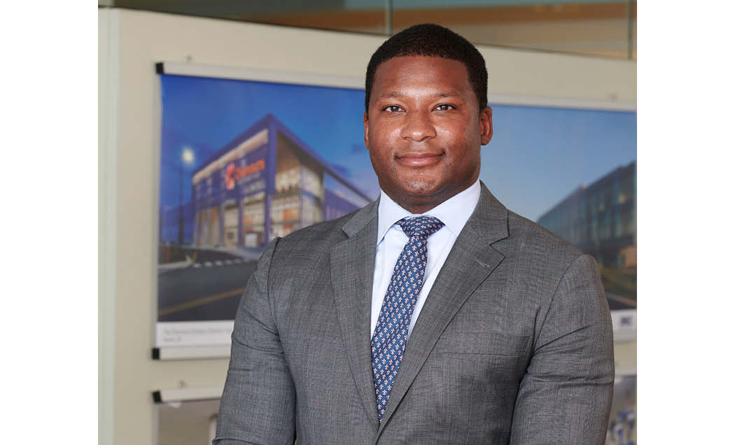 A headshot of Michael Lloyd, Chief Operating Officer at IMC Construction smiling at the camera in a gray suit with a blue tie