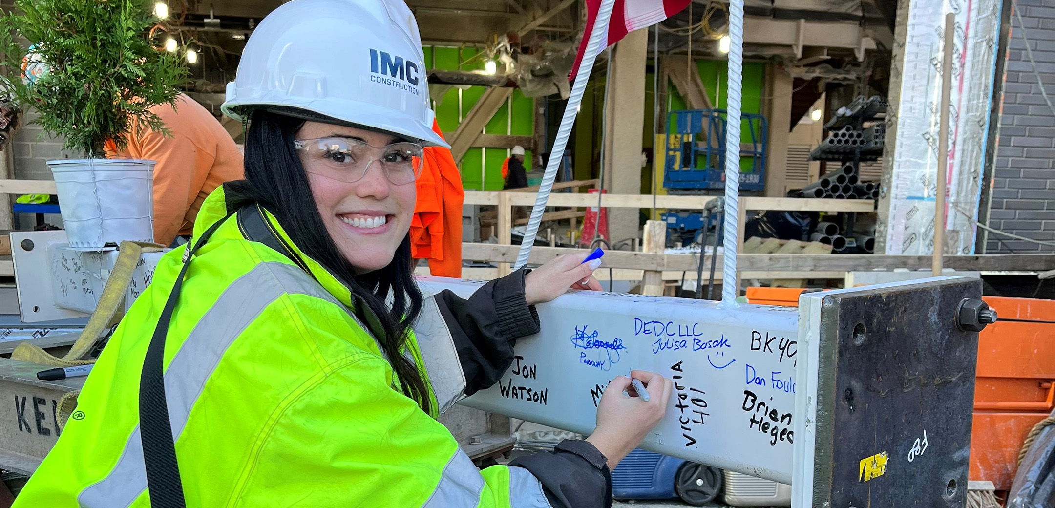 A close up of an IMC employee signing a topping off beam wearing a safety helmet and vest