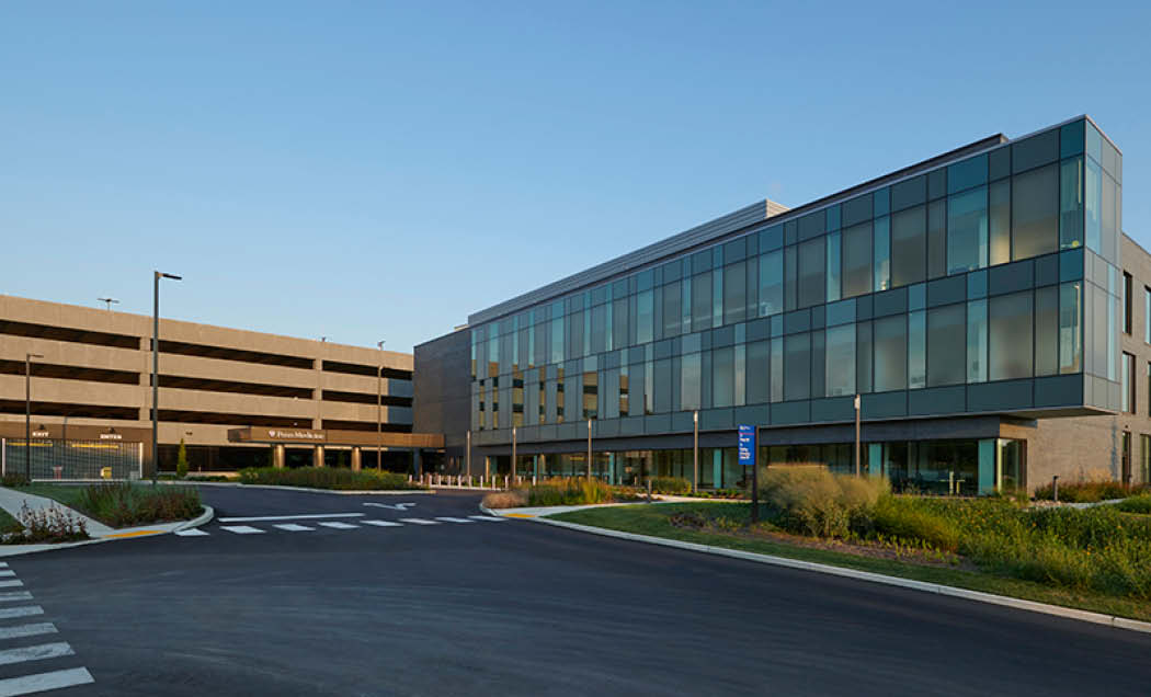An angled view a modern 3 story Penn Radnor Advanced Outpatient Care Center building showcasing the full length glass window and front driveway entrance.