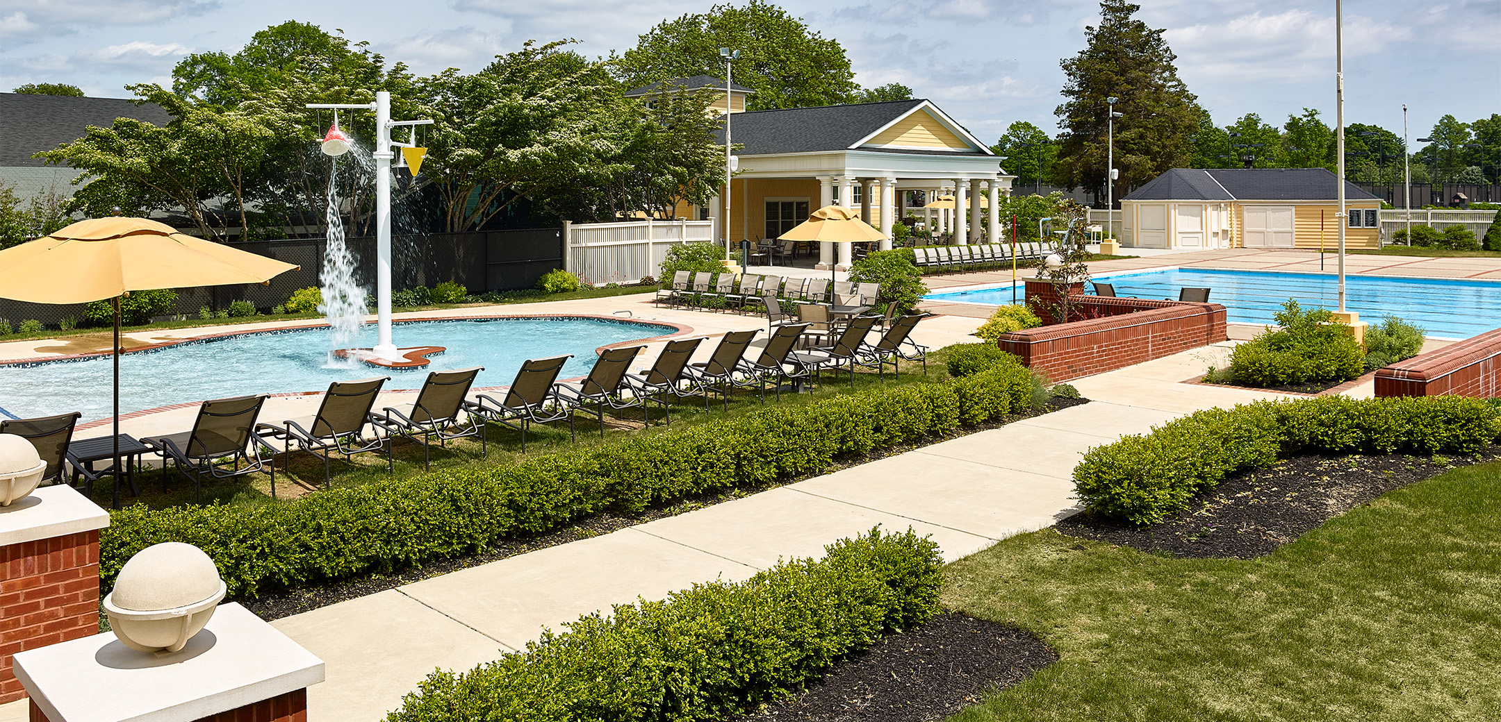 The Philadelphia Cricket Club`s outside pool featuring two large separate pools, multiple pool lounge chairs, a pool house in the far right, and the snack bar facility in the back behind the lap pool.