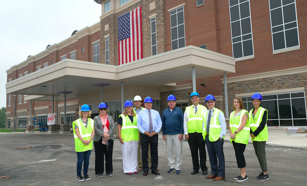 Ten project members in yellow visibility jackets and blue IMC Construction hardhats stand in front of the St. Luke's Upper Bucks Campus.
