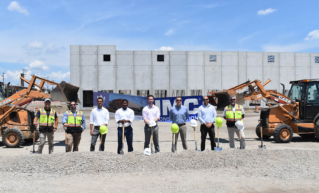 A group of IMC employees in front of the 956 E. Erie Warehouse holding shovels in their hands