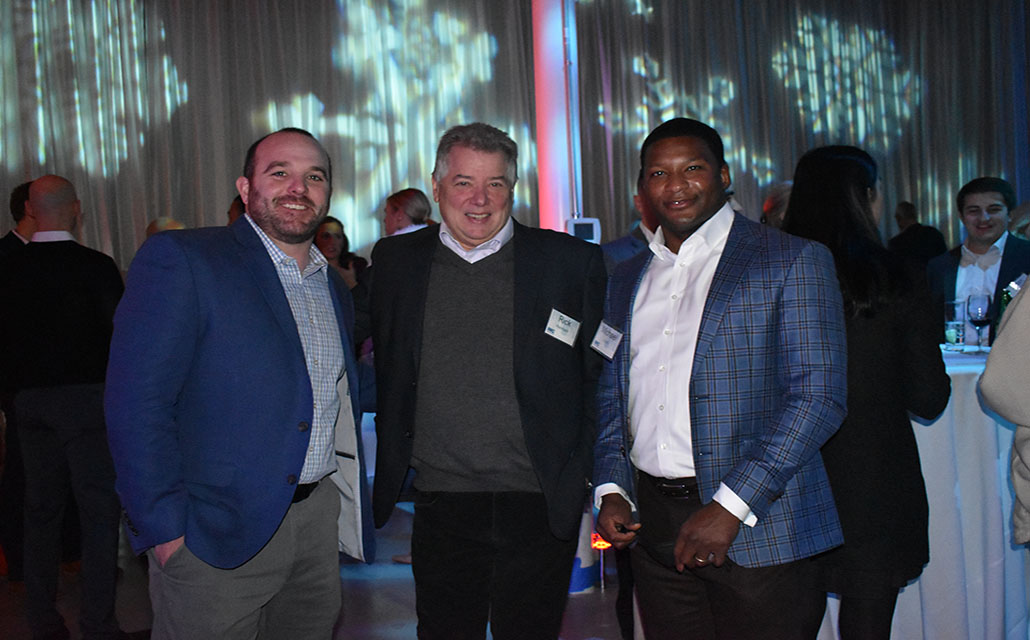 Three IMC employees wearing suits and ties posing for a photo at a company holiday party