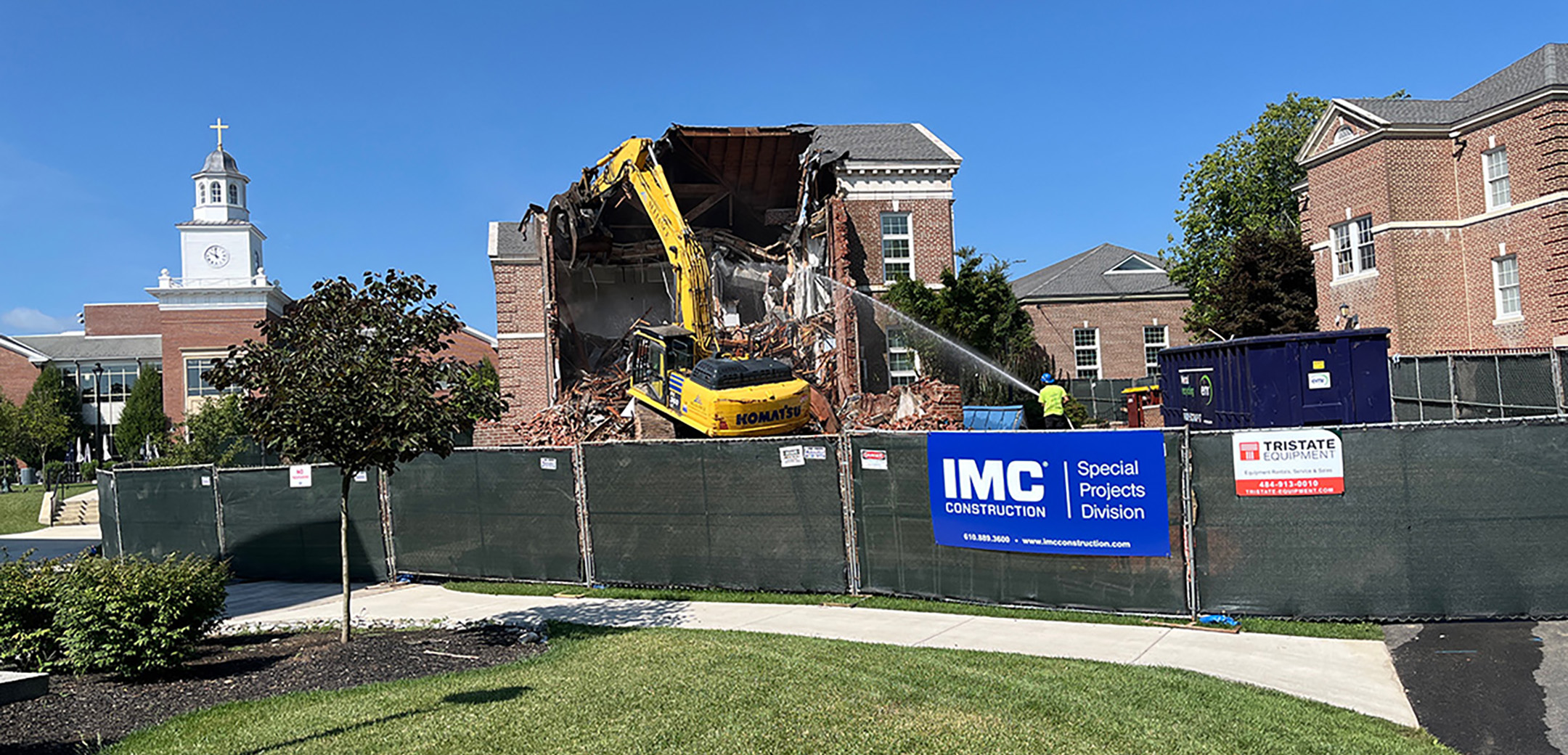 The Good Counsel Building on Malvern Preparatory's campus being being demolished with a yellow construction vehicle and green fencing enclosing the project site