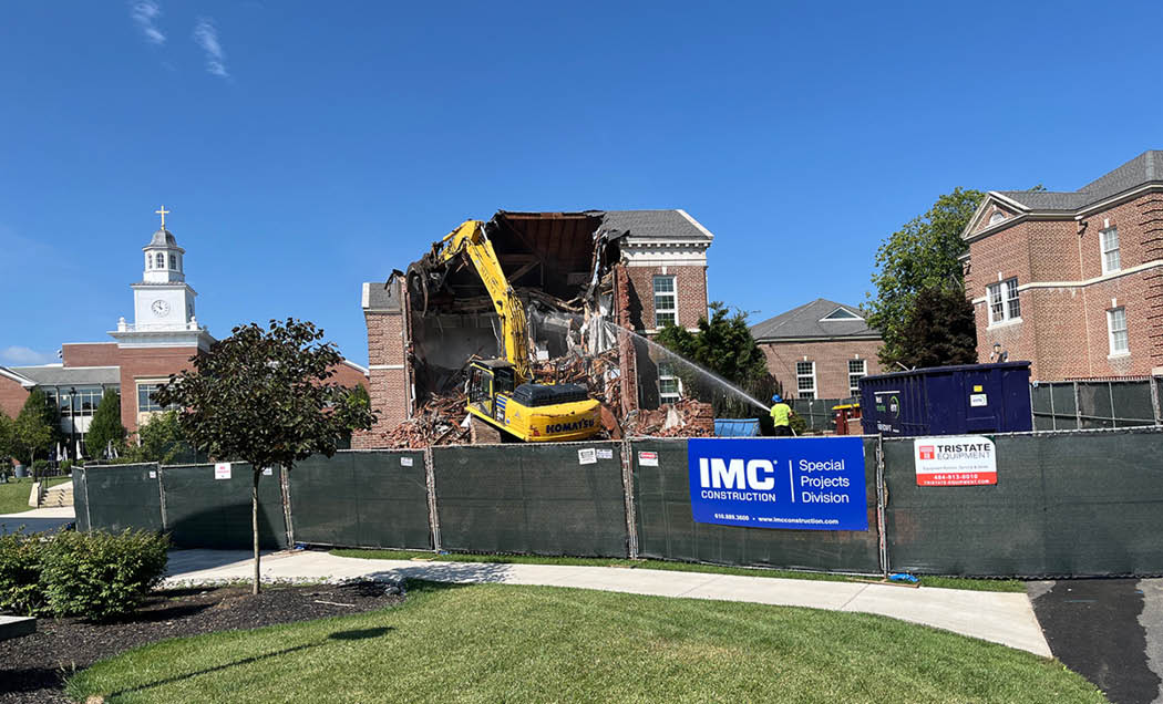 The Good Counsel Building on Malvern Preparatory`s campus being being demolished with a yellow construction vehicle and green fencing enclosing the project site