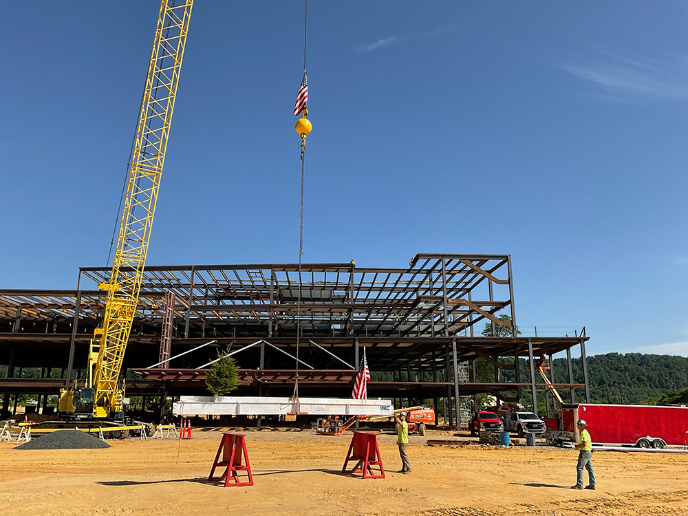 The view of Good Shepherd Rehabilitation hospital under construction with a white steel beam in front of it and a crane holding the beam