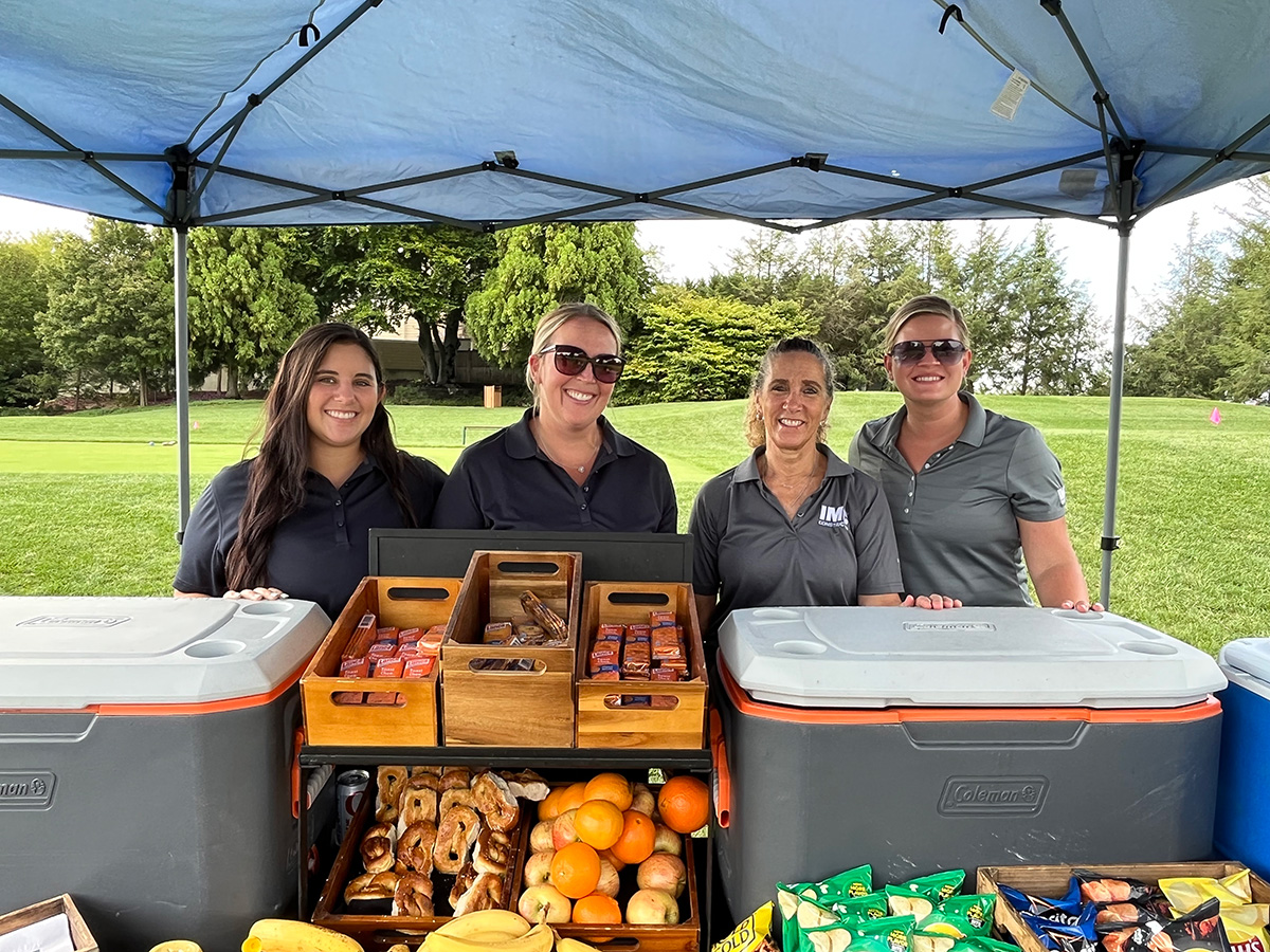 A group of women in gray golf shirts smiling for a picture behind a snack stand