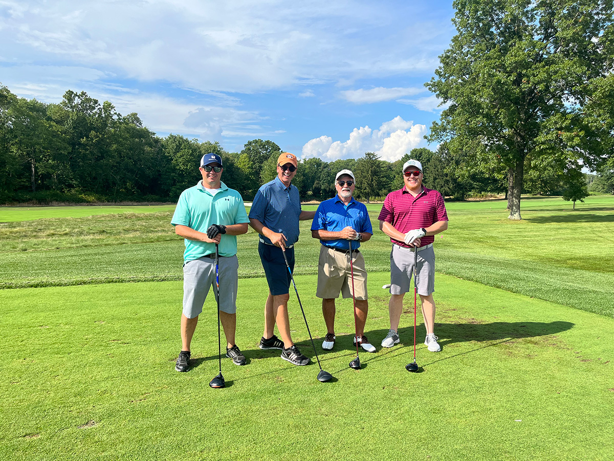 A group of golfers smiling for a picture on a green golf course